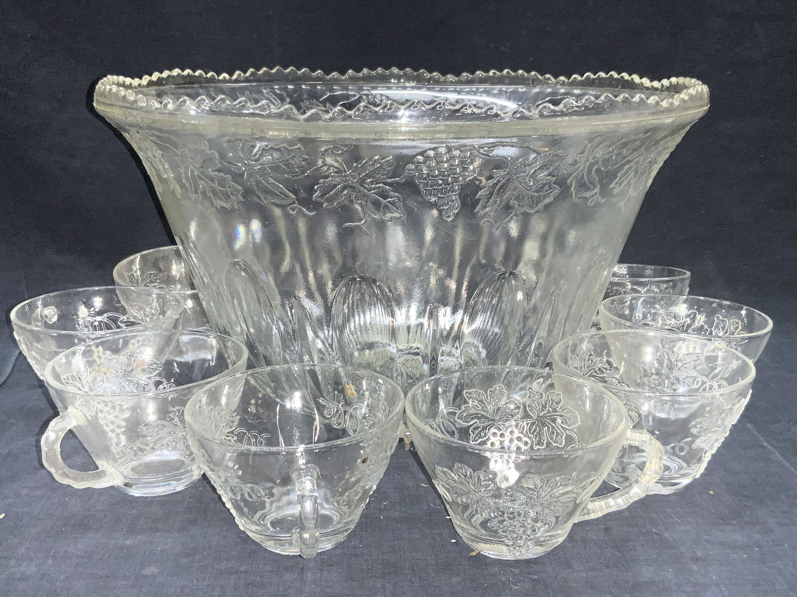 Glass Punch Bowl Service & Glass Table Accessories: Group lot consisting of 1 glass punch bowl with 8 glasses. All adorn its floral motifs on rims and exteriors. Punch bowl is approximately 7 inches tall and 12 inch diameter. 1 glass bowl with pink hue