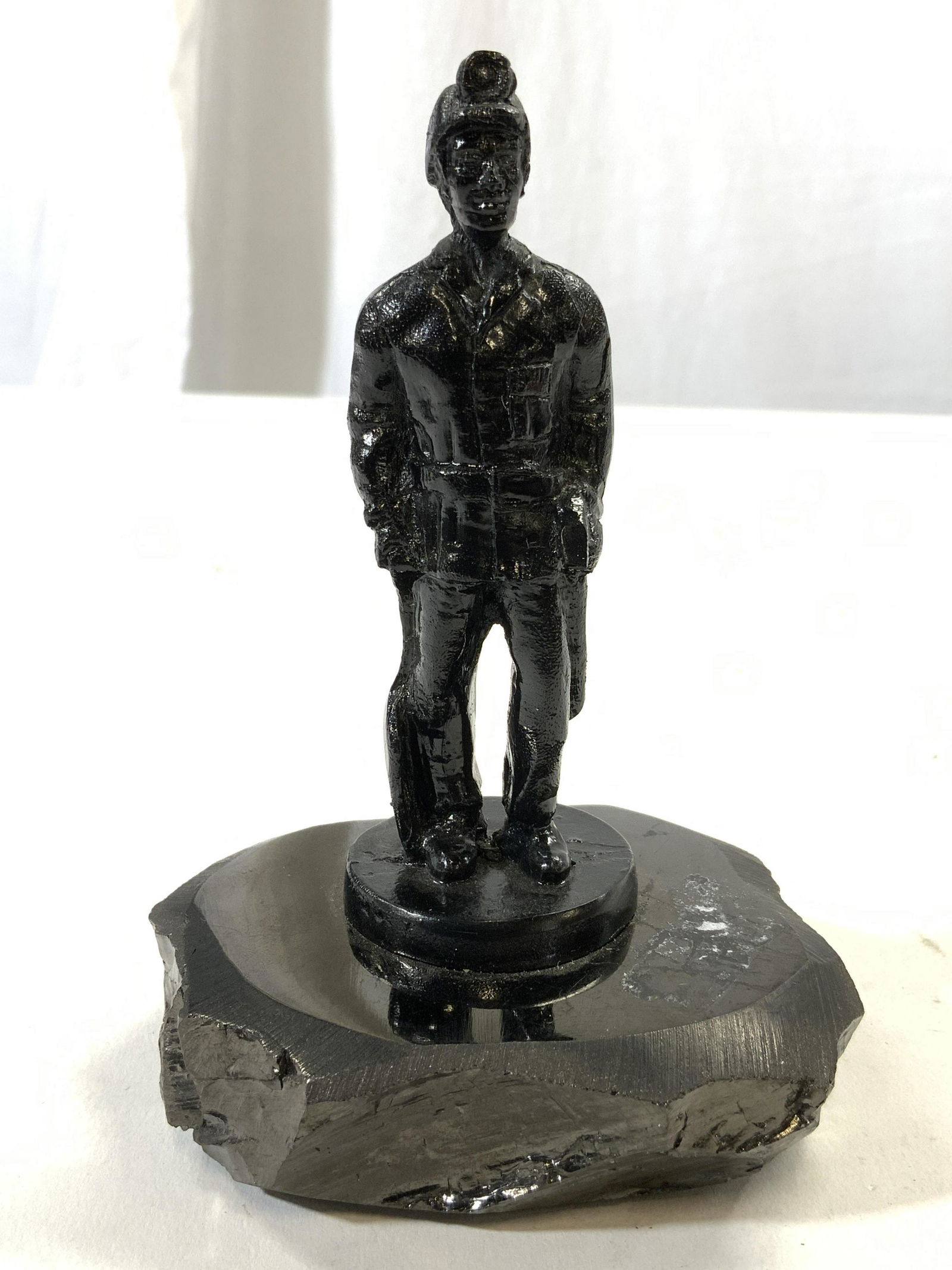 Coal Miner Statuette Figure On Coal Base: Coal miner statuette is black toned, light resinous material. Figure is affixed to polish coal base possibly obsidian. Piece measures approx 5 inches tall 3.25 inches wide 3 inches deep. Coal miner, c