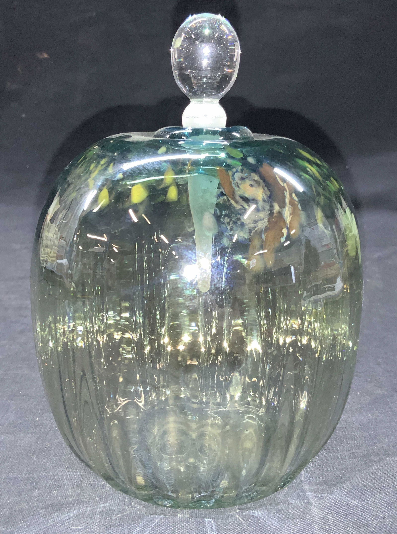 BREJCHA STUDIO Art Glass Vessel Perfume Bottle: Etched on underside BREJCHA. Art glass vessel / perfume bottle in green and blue tones with speckles of yellow with clear glass and frosted glass stopper. Approximately 7 inches tall. Minor wearing to