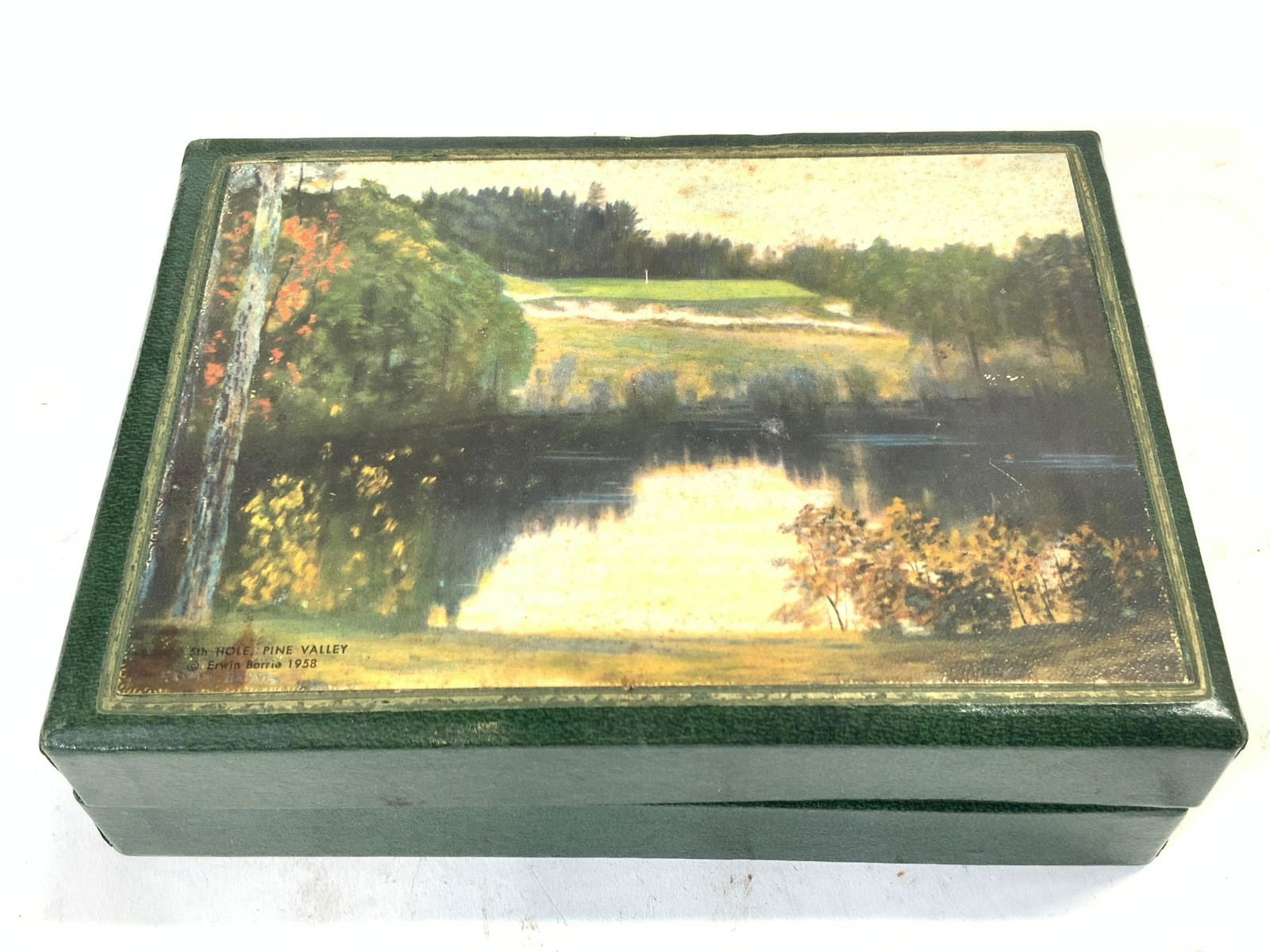 SPALDING Brand Golf Motif Box: Marked on interior SPALDING, with a silhouette of a man playing golf Green toned box with lithograph printed on top of lid depicting a landscape of a golf course, marked on left corner 5th hole, Pine