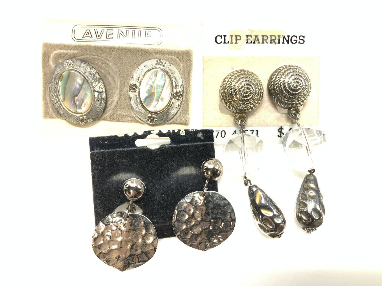 3 Pairs of Clip On and Pierced Earrings, NIP: New old stock earrings, on original store packaging. Clip on hammered silver toned metal discs, 1.5 in L x 1 in. Wide, 3 in. L clear bead and silver tone clip on earrings. Oval mother or pearl and sil
