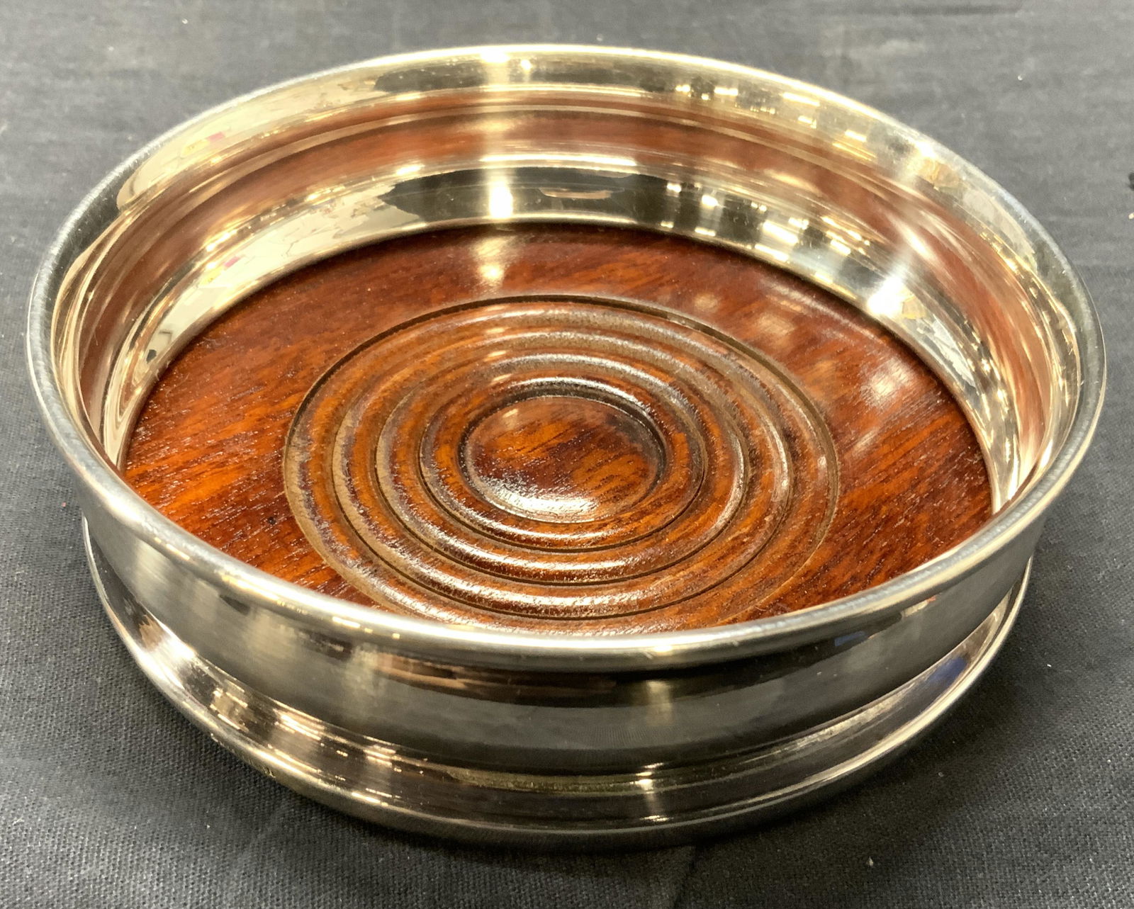 GAINSBOROUGH ENGLAND Silver Plated Wine Coaster: Wine coaster is inscribed GAINSBOROUGH ENGLAND SILVER PLATED. Wine coaster is silver plated, interior is brown toned & wooden. Piece measures approx 5.25 inches diameter. Some scratches and discolorat