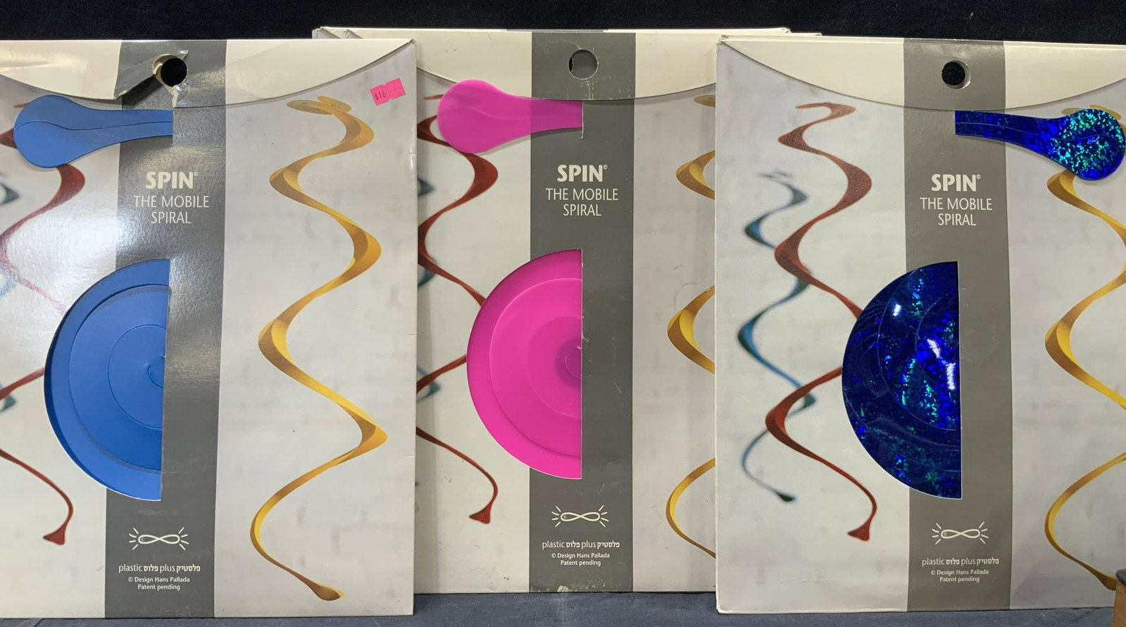 10 SPIN Mobile Spirals, In Original Packaging: Set of 10 hanging ceiling spirals in original packaging. Colors range from blues, glitter blue, and pinks. None opened Packaging is approximately 15 x 13 inches, Evident wearing to paper packaging. Sp