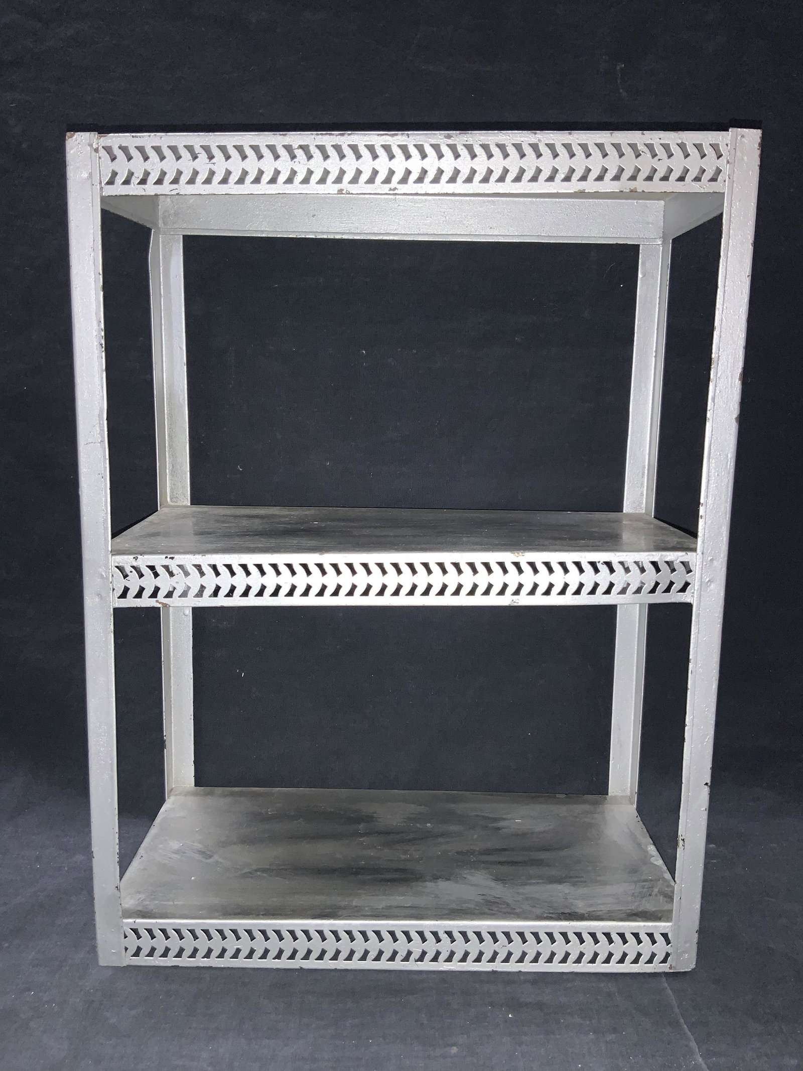 16 Inch Three Tiered Metalwork Shelf: Three tiered metal work shelf, painted silver. Made to resemble industrial shelves. Approximately 16 inches tall and 12 inches long. Evident wearing to paint and metal. Shelving, tabletop shelf, metal