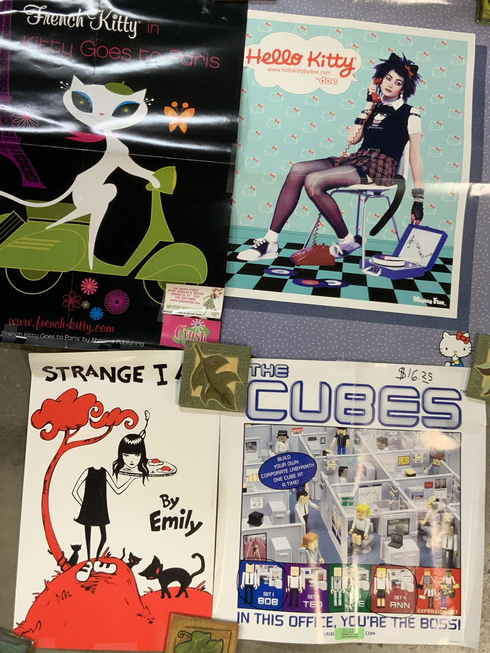 6 Pop Culture Adverts Hello Kitty, Emily & More: Group lot of 6 pop culture advertisement posters. Consisting of hello Kitty, Kitty goes to Paris, Cubes, 2 posters by Emily is Strange and Oopsy Daisy. Largest poster is approximately 24 x 18 inches.