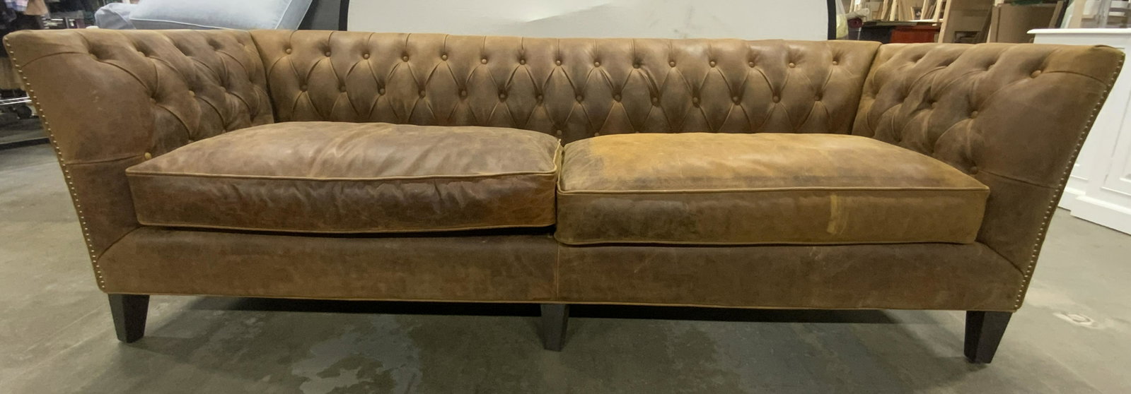 UNIVERSAL EXPLORE HOME Leather Chesterfield Sofa: Underneath cushion has tag which reads UNIVERSAL EXPLORE HOME. Sofa os brown toned & appears to be leather. Piece has gold toned nailhead detail at some edges. Back and armrests are tufted. Sofa measu