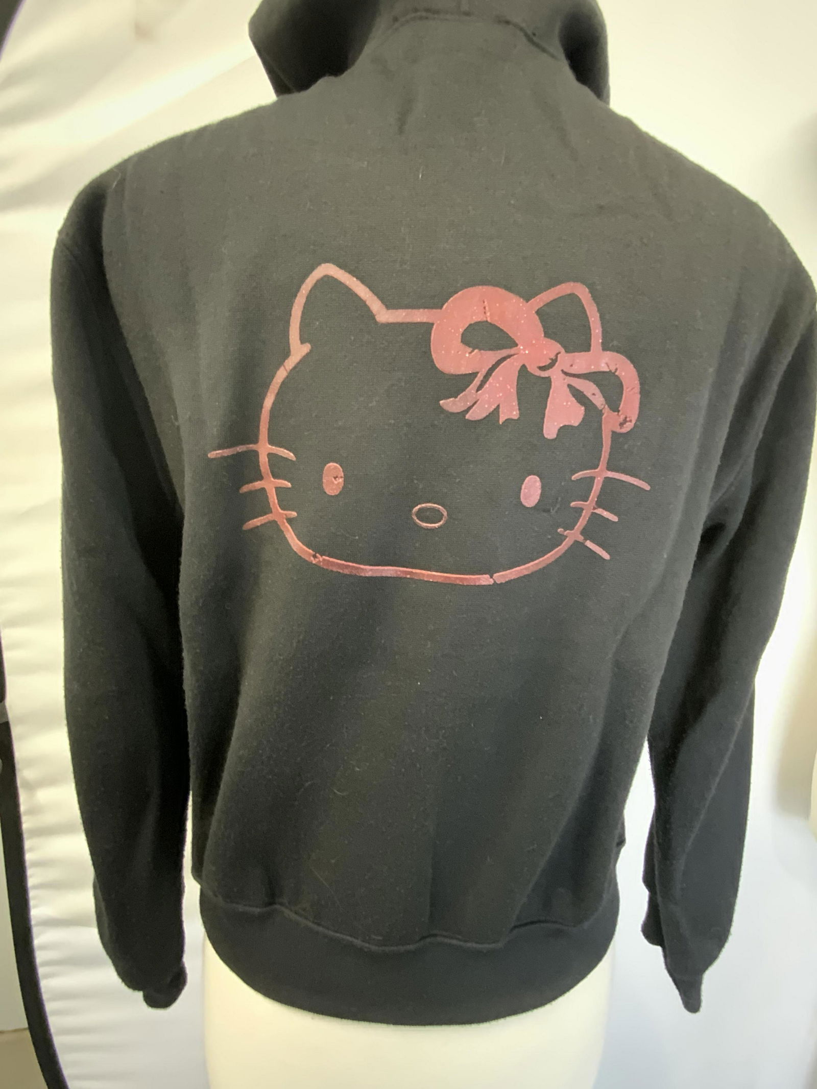 THE SANRIO COLLECTION HELLO KITTY Zip Up Sweater: A black zip up hooded sweater. Silver tone metal stud details. Obverse reads Hello Kitty. Reverse features the iconic Hello Kitty face. Pockets to obverse. Tag reads THE SANRIO COLLECTION, size Large.