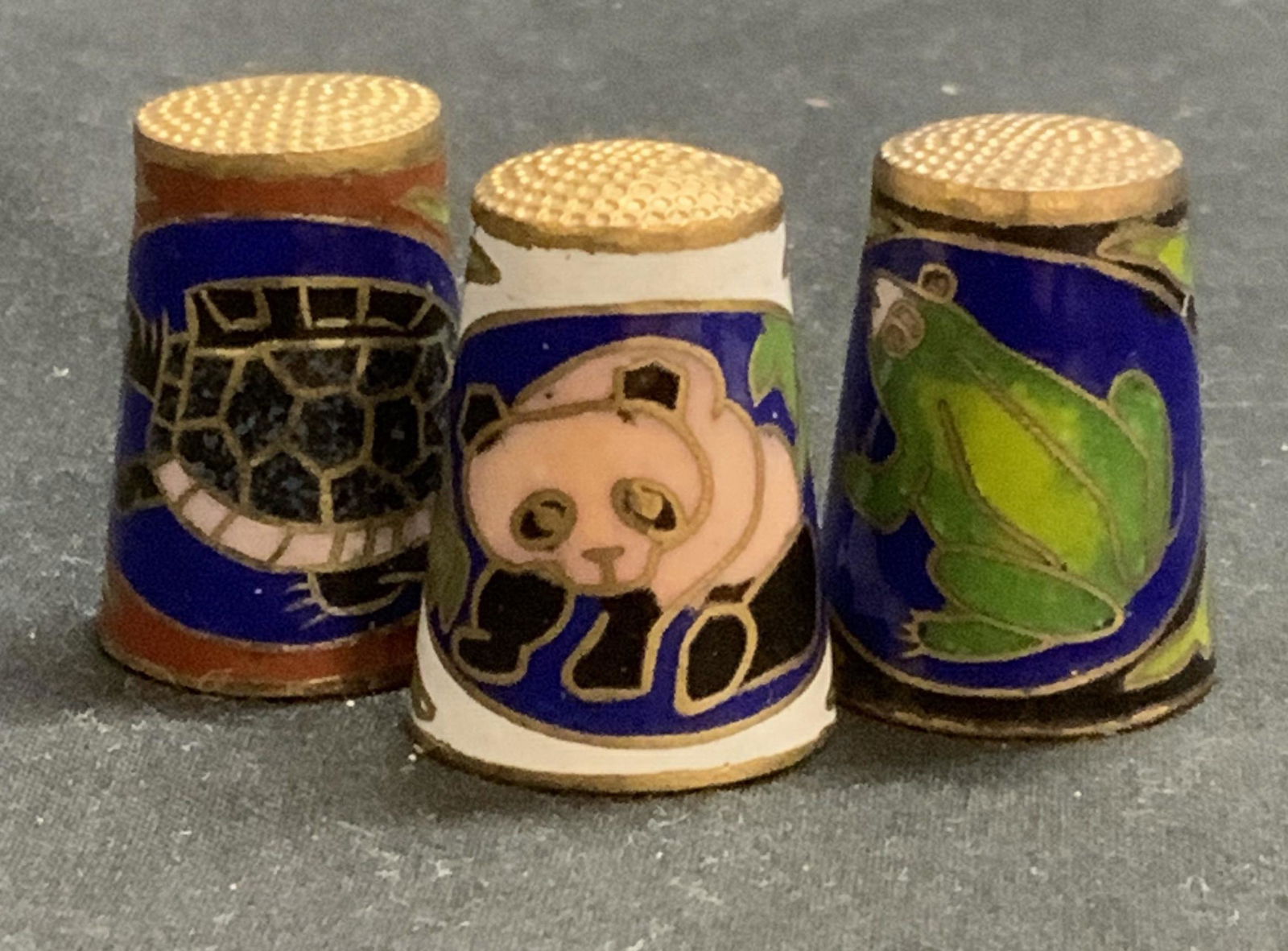 Lot 3 Cloisone Thimbles w Animal Motifs: Lot of 3 cloisonne thimbles with panda, frog, and turtle motifs. Enamel on brass. Surface wear to all pieces consistent with exposure. Measure approx. .75 inches diameter and 1 inch tall each. Thimble