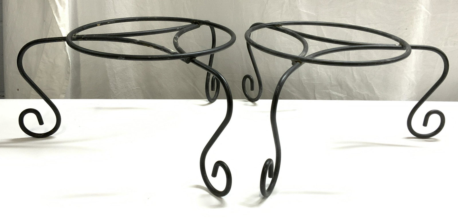 Pair Iron Jardiniere Planter Stands: Pair of black iron jardiniere/planters stands. Surface wear to both pieces consistent with exposure. Measure approx. 12 inches diameter at center, 17 inches wide, and 8 inches tall each. Planter stand