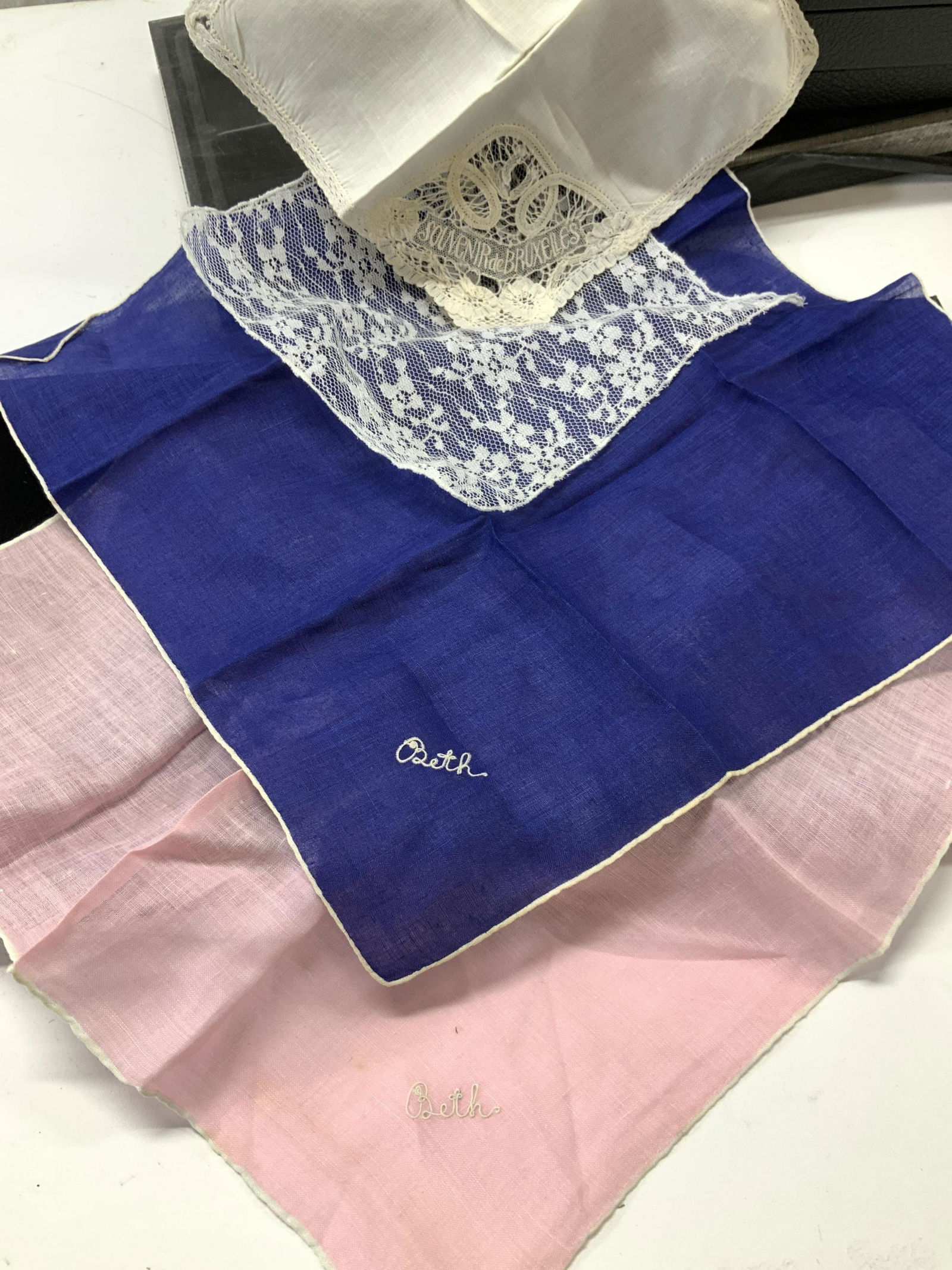 4 Colored Linen Hankies, Lace, Brussels: Royal blue and pink linen handkerchiefs with white hand rolled edging . Both monogrammed Beth measure 12 x 12 in. White lace Hankie, cream toned linen Hankie with lace edging and embroidered Souvenir
