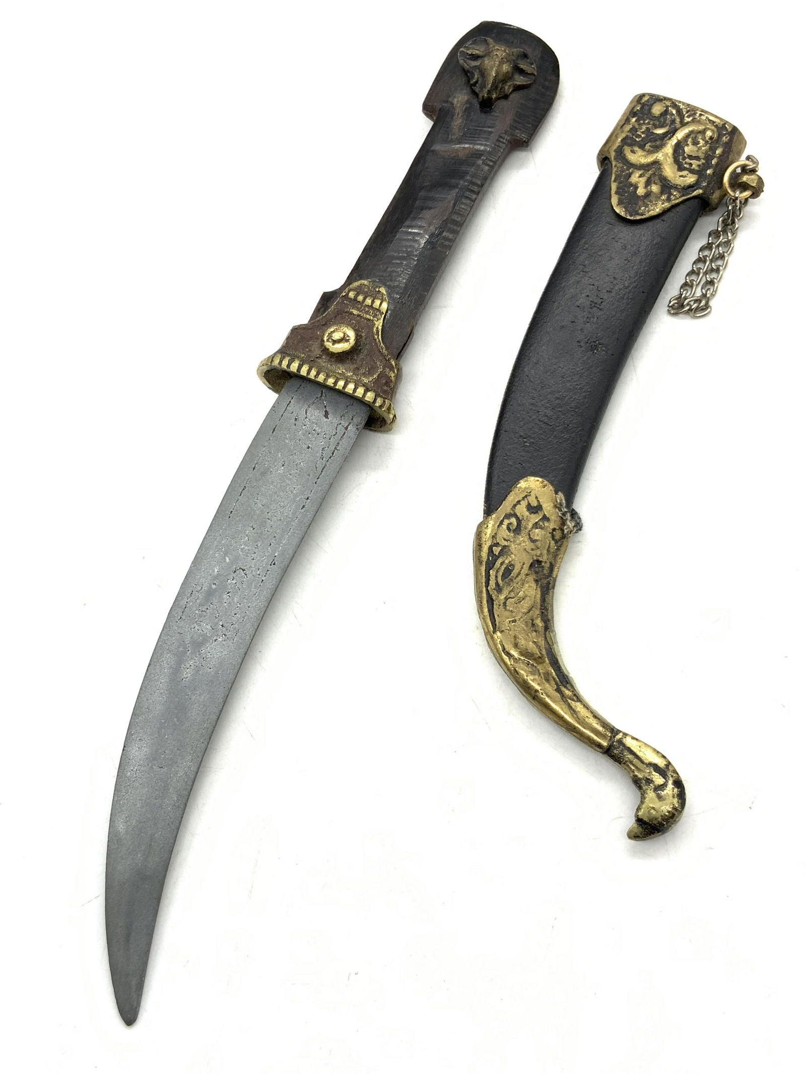 Vintage Brass & wooden Scabbard Dagger: Vintage curved blade dagger with scabbard made of black leather and etched brass capped ends. End cap has head that resembles a goose or duck. Handle is carved bone with finish, and affixed brass made