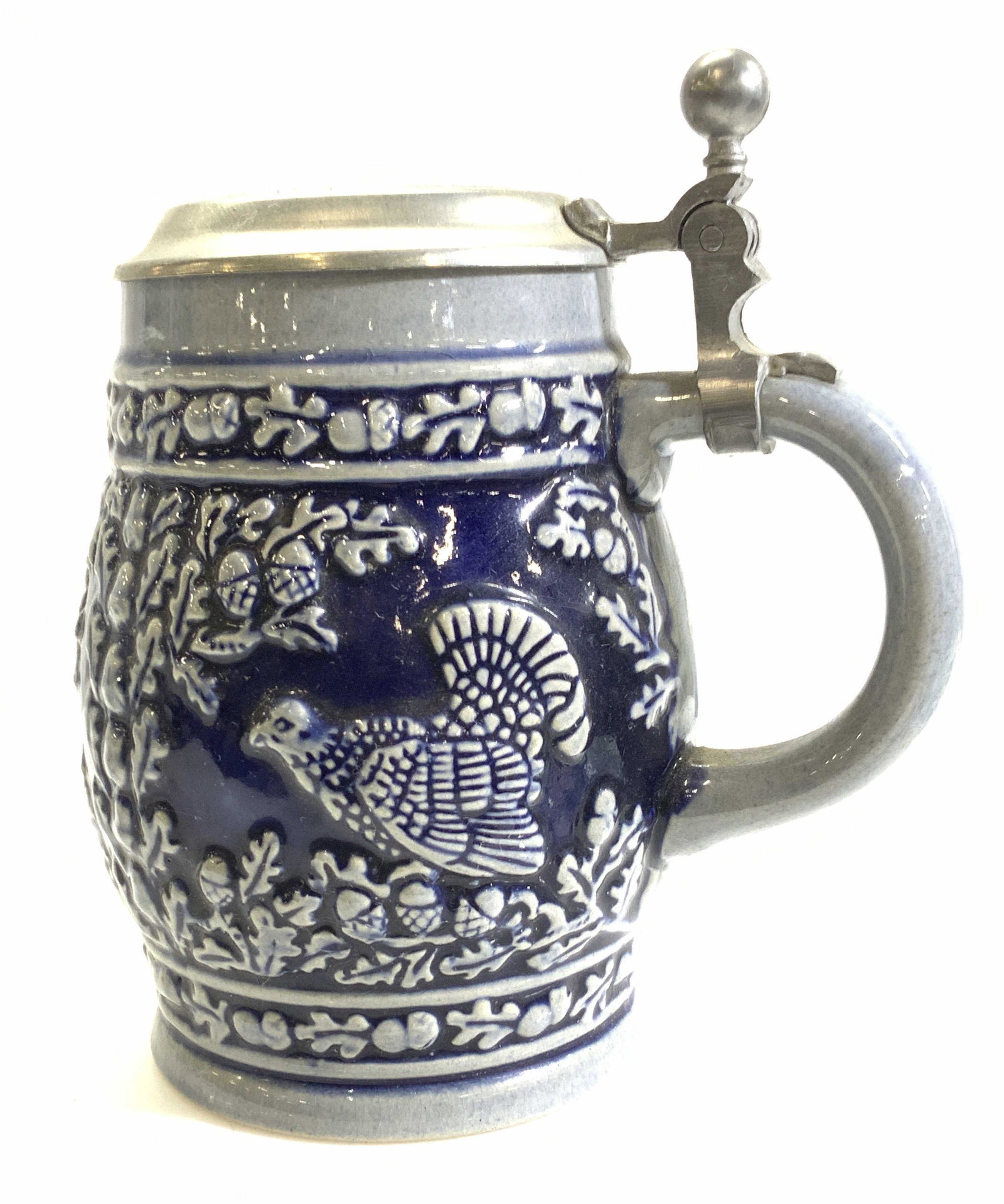 MR Porcelain Tankard W Stag, West Germany: Signed Tankard, glazed cobalt blue with high relief of stag , Turkey, and pheasant with Reticulated decor of oak leaves and acorns. Flip up top, hallmarked MR Zinn. Underside reads MR West Germany. Ve