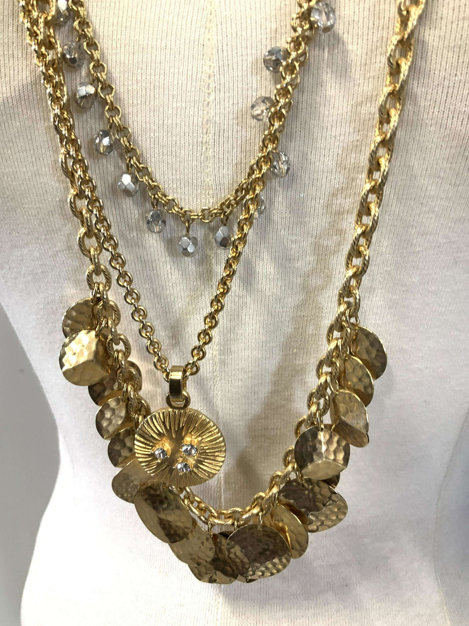 YOSCA 28 in. Gold Tone Multi Chin Necklace: Signed designer YOSCA. triple chain necklace, polished and diamond cut chains, hammered disc charms on one chain, faceted clear beads on another chain, medallion pendant with 3 prong set crystals. 28 