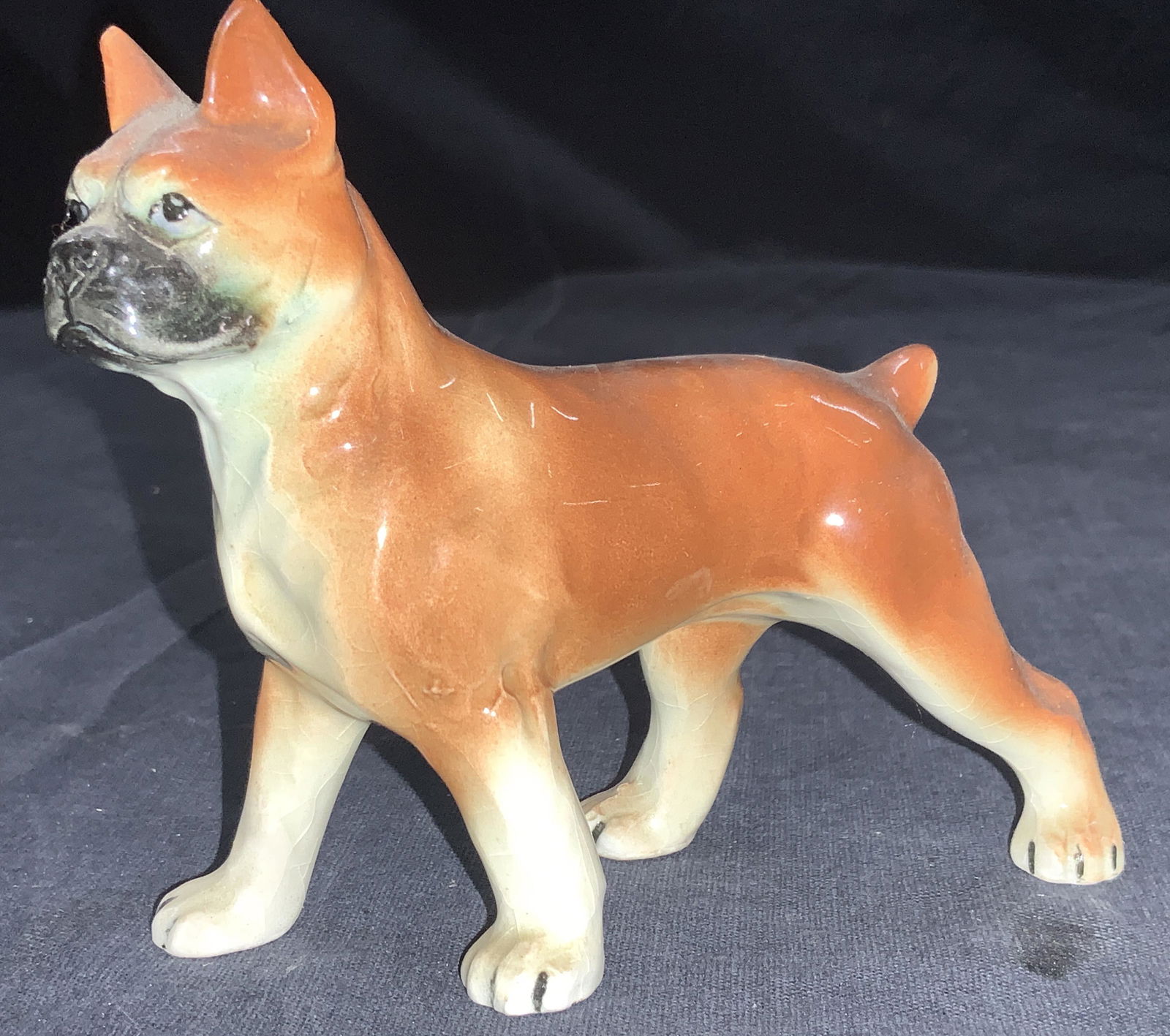 Ceramic Made Boxer Dog Figurine: Ceramic figurine made To resemble a boxer dog with brown tone glazing and pointed ears. Approximately 3.5 inches tall and 5 inches long. Evident crazing to ceramics and undersides. Ceramic dog figurin