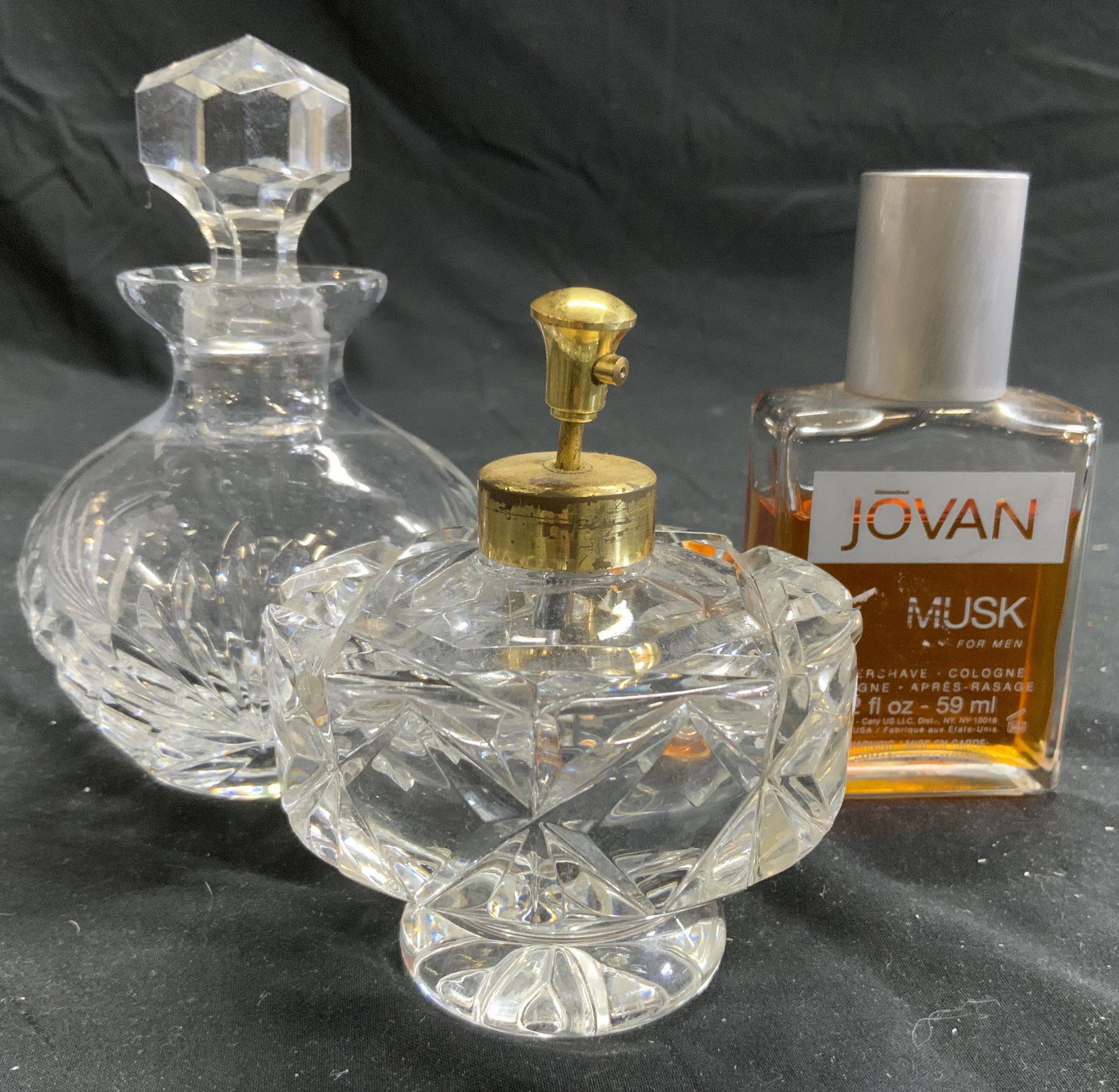 Lot 3 Glass & Crystal Fragrance Bottles: Lot includes 3 fragrance bottles. 2 appear to be crystal 1 is glass. Glass bottle is partially full reads JOVAN MUSK AFTERSHAVE COLOGNE and includes cap. 1 bottle has decanter shape & includes stopper