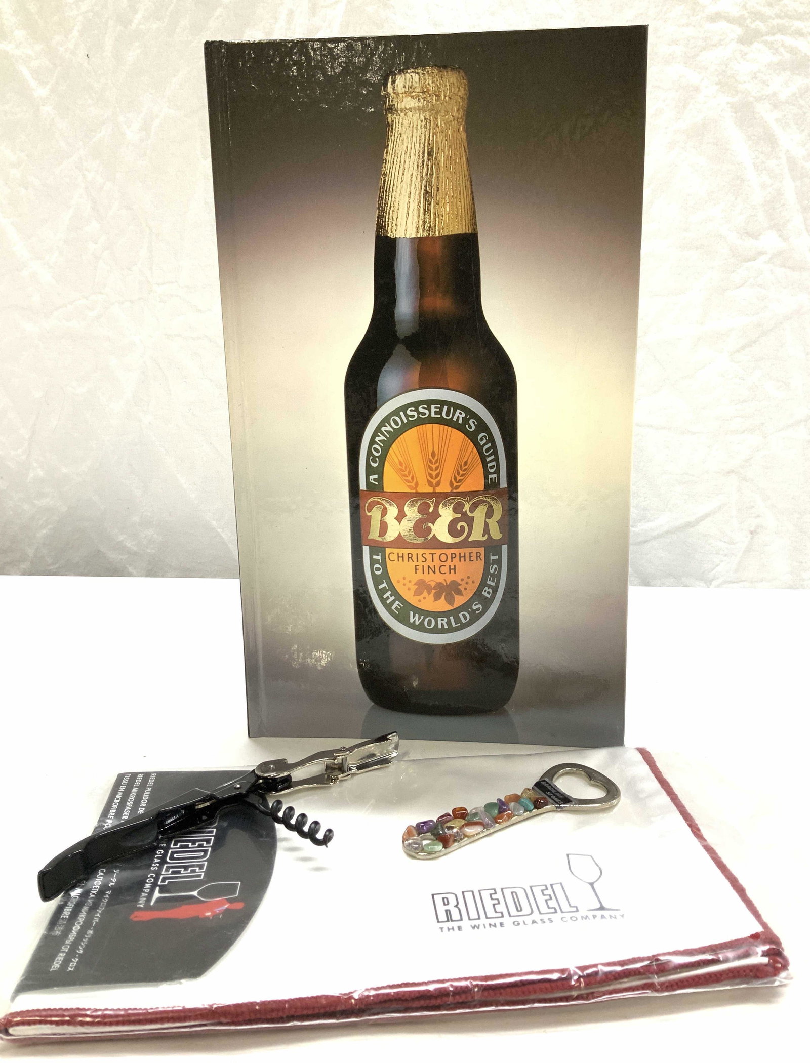 Lot 4 Beer Connoisseur Book & Bottle Openers: 2 bottle openers, one pop cap top bottle opener with Quartz gemstones from Brazil , measures 4 in. True tap cork bottle opener, 4.5 in long. New in package RIEDEL wine glass co microfiber polishing cl