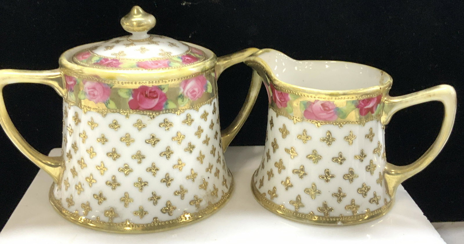 Hand Painted Porcelain Creamer, Sugar Bowl: White Fine bone China with hand painted roses and gilt. Marked Nippon on verso. Creamer measures 3 x 4.25 in. Ht x W Sugar bowl with lid measures 6 x 3.5 in. W x Ht Light gilt wear. Needs cleaning Por