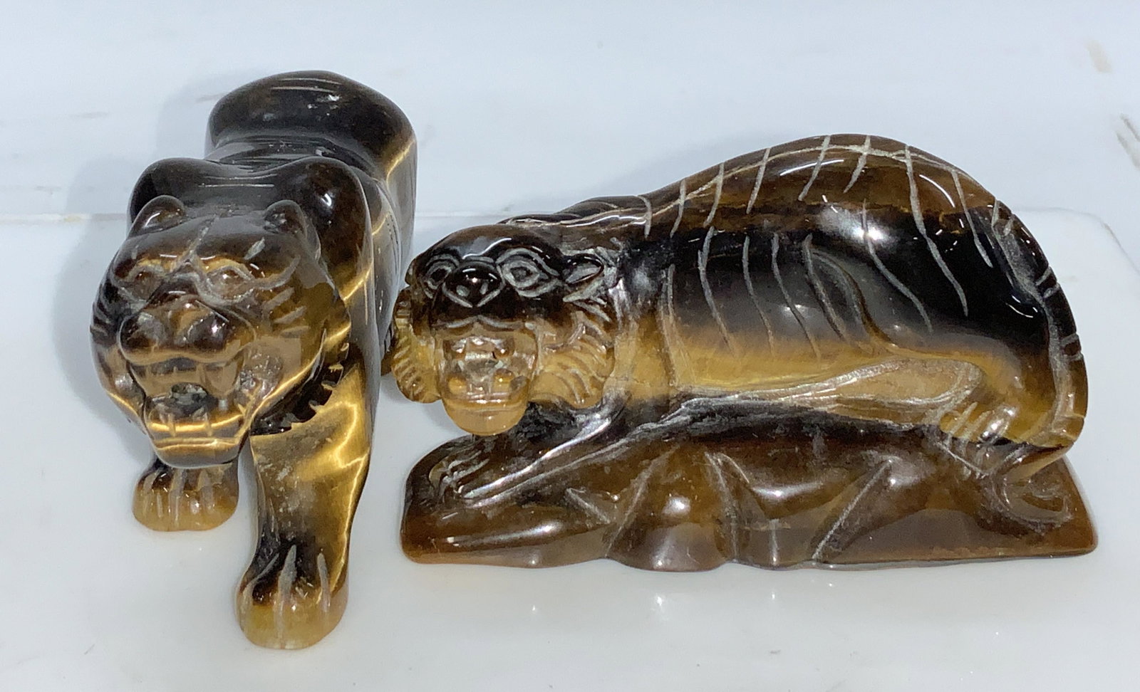 Pair Carved Tigers Eye Lioness Figurines: Carved and polished natural gemstone lion and guardian Temple lion figurines made of solid Tigers Eye.. Measures 4.25 x 2 in. and 3.25 x 2 in. 1561 ctw of gemstone. Crack on temple lions body possibly