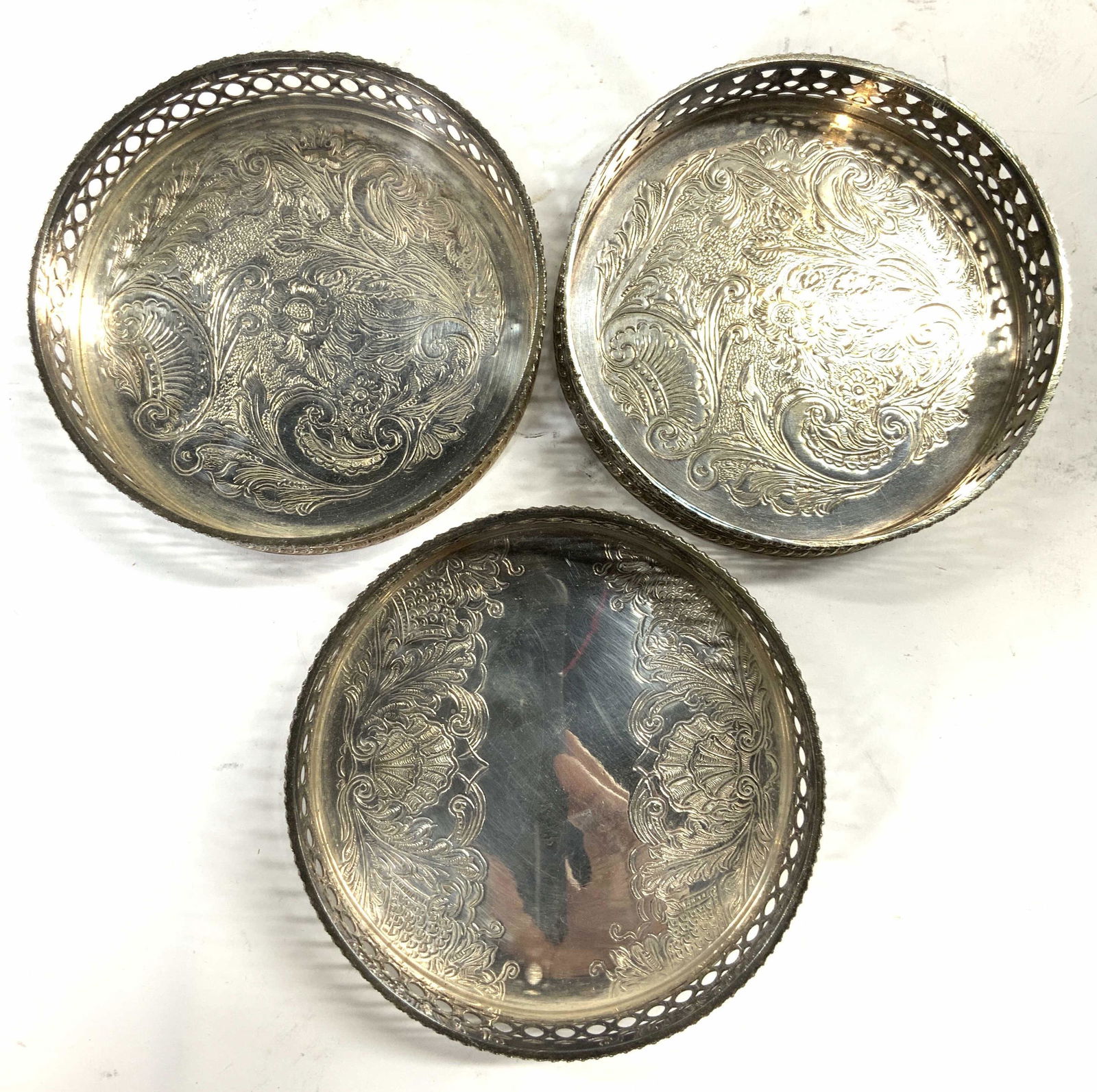 SHEFFIELD SILVER PLATED Lot 3 Wine Coasters: Lot includes 3 wine coasters. Each are inscribed SHEFFIELD SILVER PLATED. Each coaster differ slightly. Each piece has scrolled ornate relief detail & pieced galleries. Each measures approx 4.5 inches