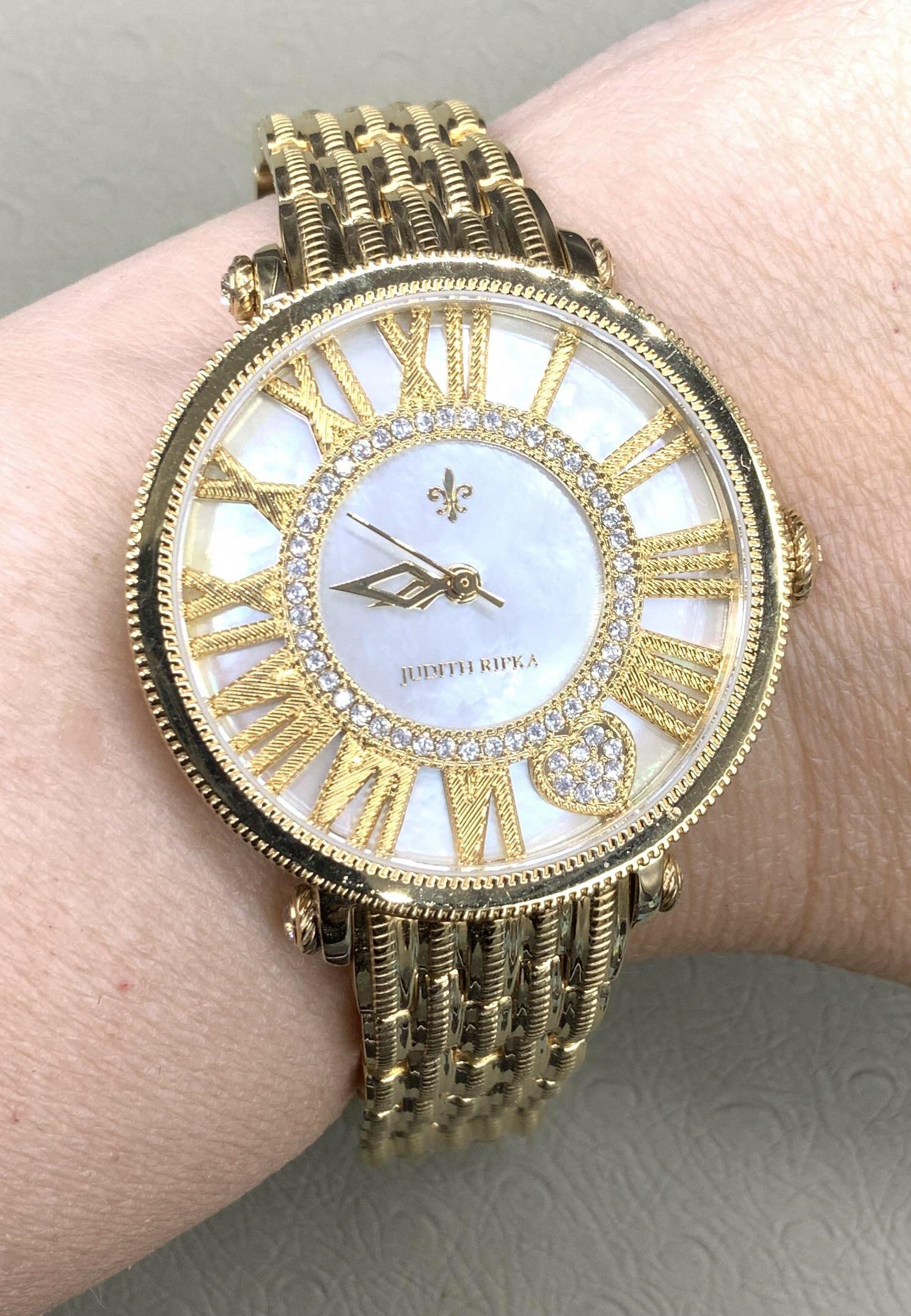 JUDITH RIPKA SGN MOP Gold Tone Watch, Box: Judith Ripka Deployment Buckle Watch in gold tone, diamond cut and polished metal. Stainless steel back, watch face with Roman numerals set on mother of Pearl. Japan movement, water resistant. Watch c