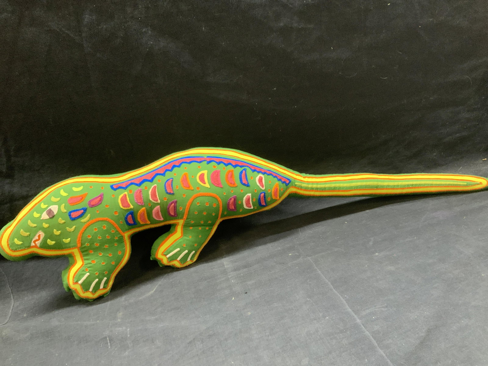 Iguana Animal Design Throw Pillow: Animal throw pillow made to look possibly like an iguana, green in tone with colored outlines in orange and yellow with colored patchwork scales and features. Approximately 29 inches long. Minor weari
