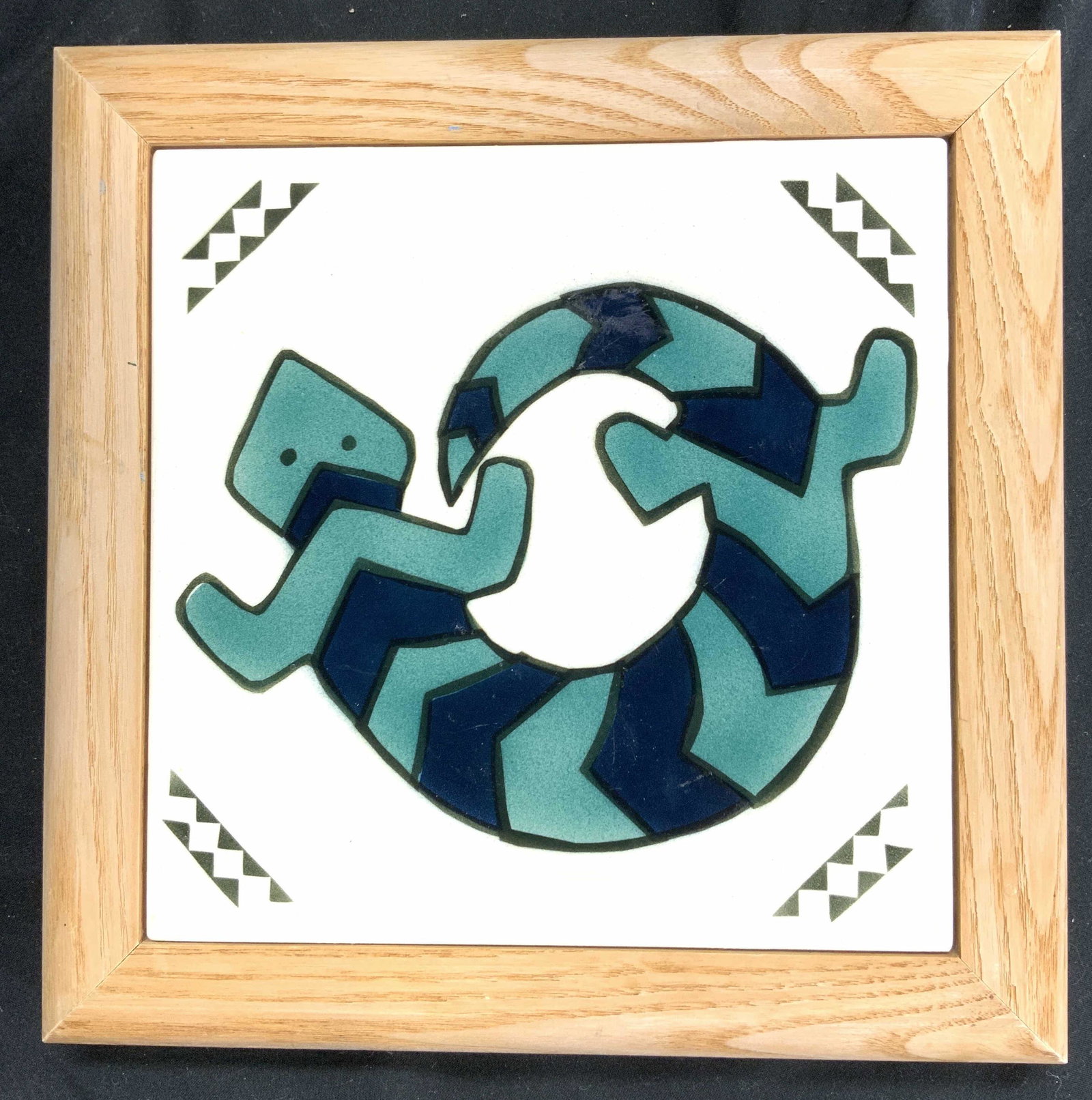 Framed Porcelain Tile W Striped Lizard: Backside of piece reads HANDCRAFTED BY PHOENIX STUDIO GALLERY. Tile is framed. Piece is porcelain with striped lined and geometric detail. Tile has tan toned wooden frame. Frame measures 7 3/4 in, squ