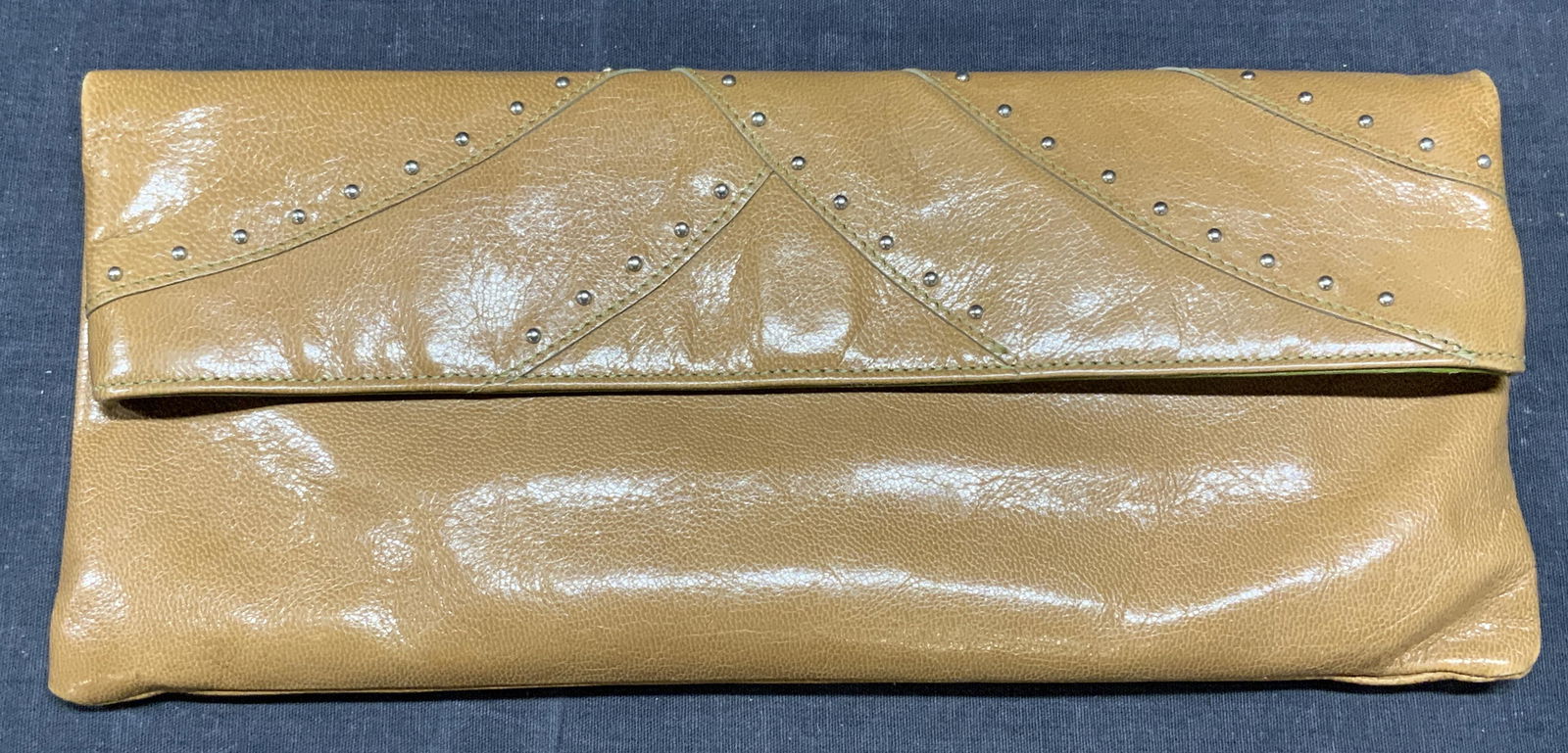 TUSK Studded Brown Leather Clutch Handbag: Tusk brown leather clutch purse with stud decoration. Fold over flap, snap button closure, 1 zippered pocket to exterior, 1 zippered pocket and 1 slip pocket to interior, designer label to leather pat