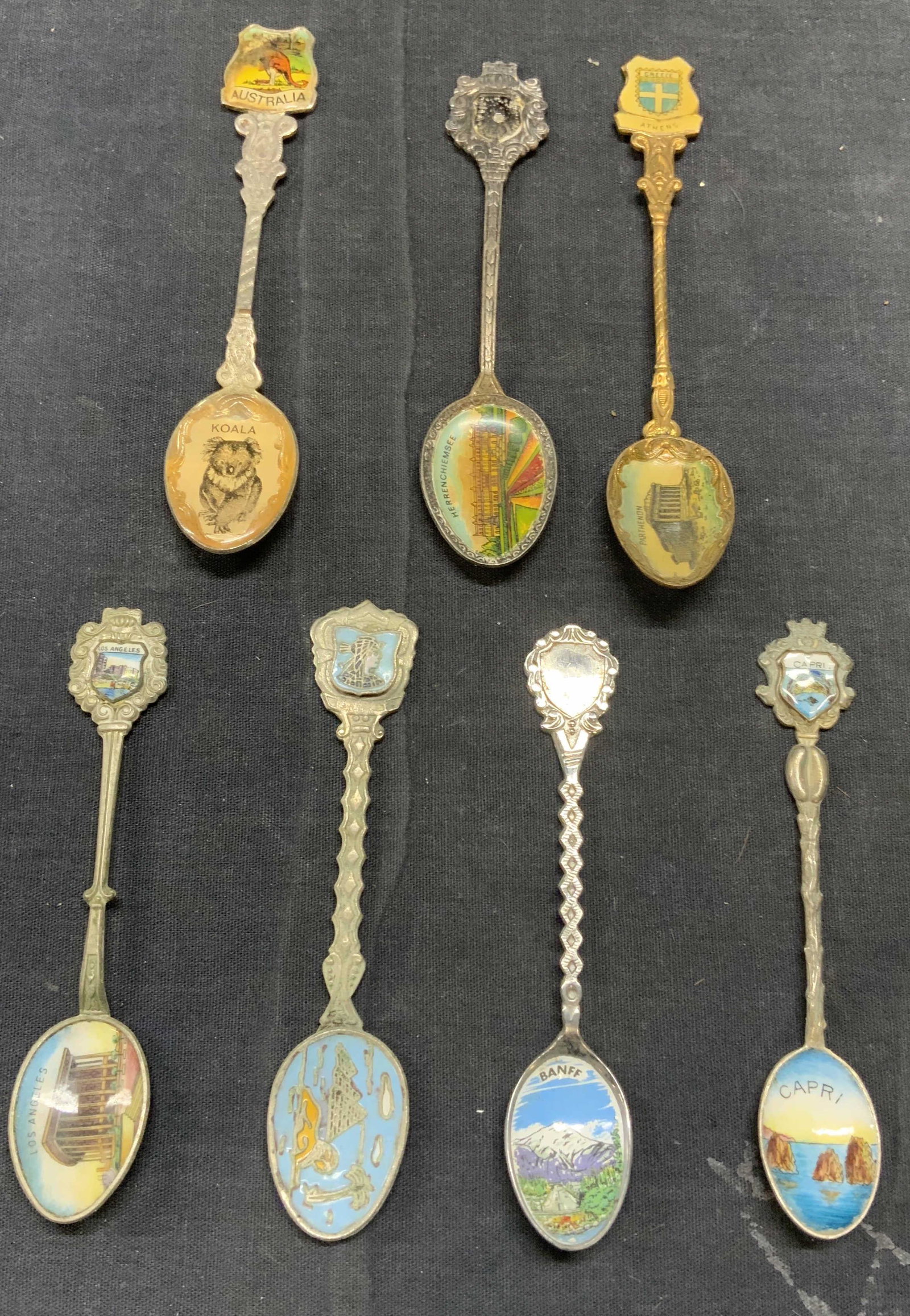 Lot 7 Collectible Vintage Enamel Spoons, Travel: Lot of 7 collectible vintage enameled travel ephemera spoons. Includes, Greece, Australia, Herrenchiemsee, Los Angeles, Egypt, Banff, and Capri. Surface wear to all pieces consistent with exposure. La