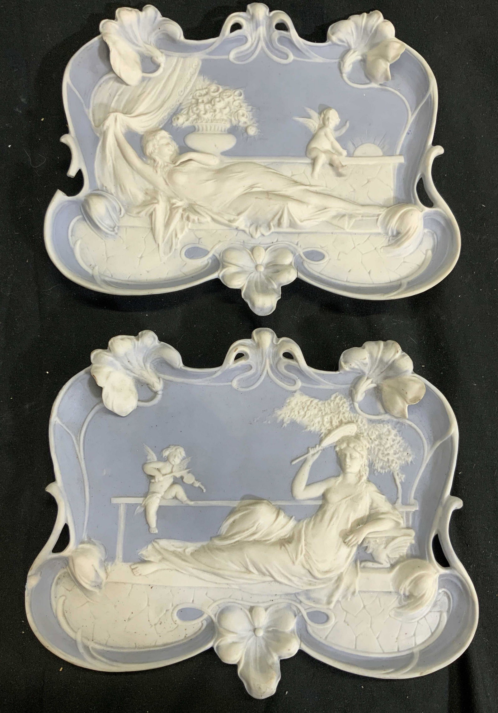 Lot 2 Vintage Jasperware Trays: Lot includes 2 Jasperware trays. Each are light blue and cream toned. Each have different depictions of laying female figures with cherub figures & floral detail. Each measures 9.75 inches long 8 inch