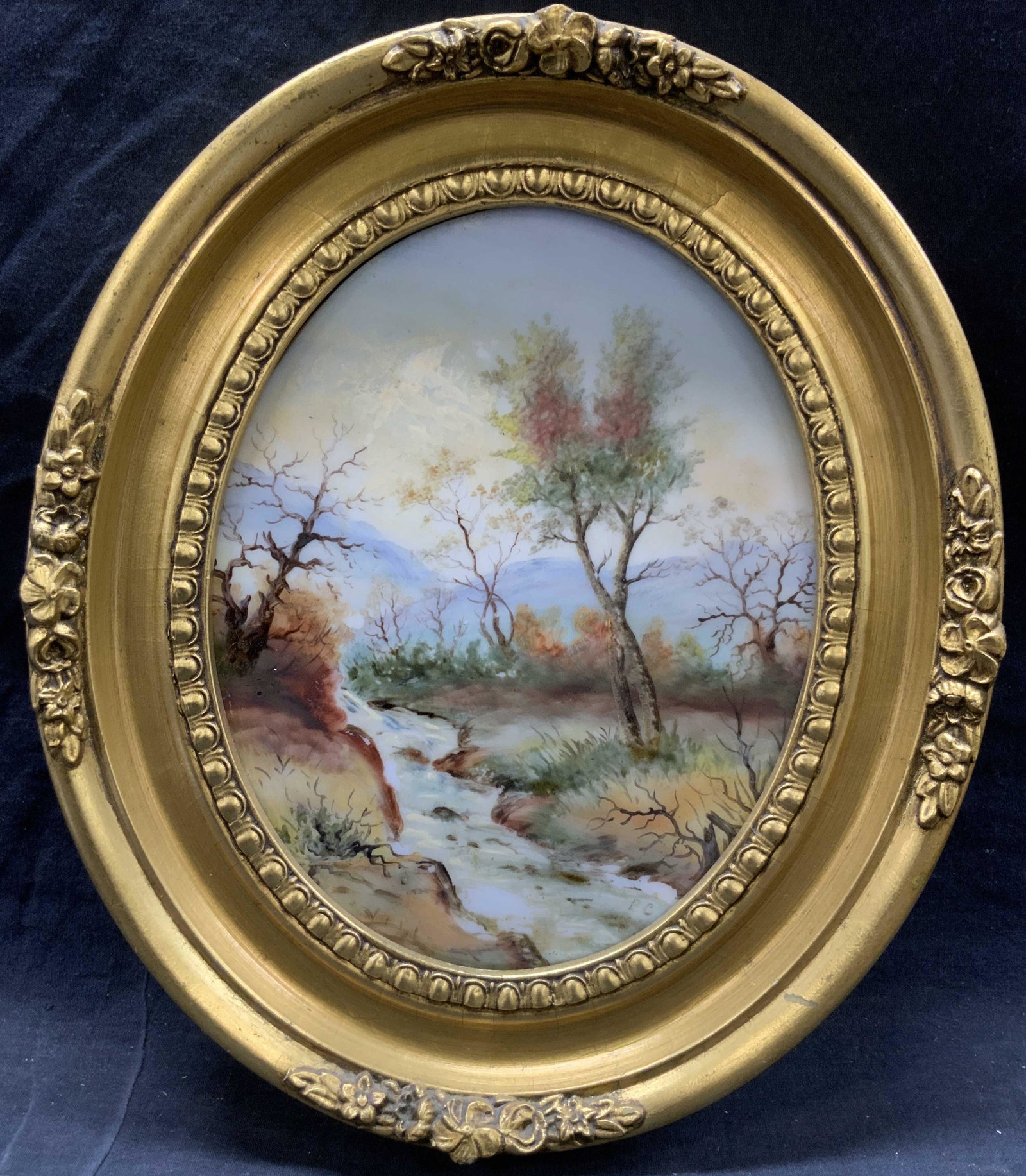 B.C. Signed Landscape Oil Painting On Tile: Signed in lower right corner B.C. Subject depicts a forest landscape with a brook going through the center to of the painting and blue mountains in the background. Framed in gold leafed wooden oval sh