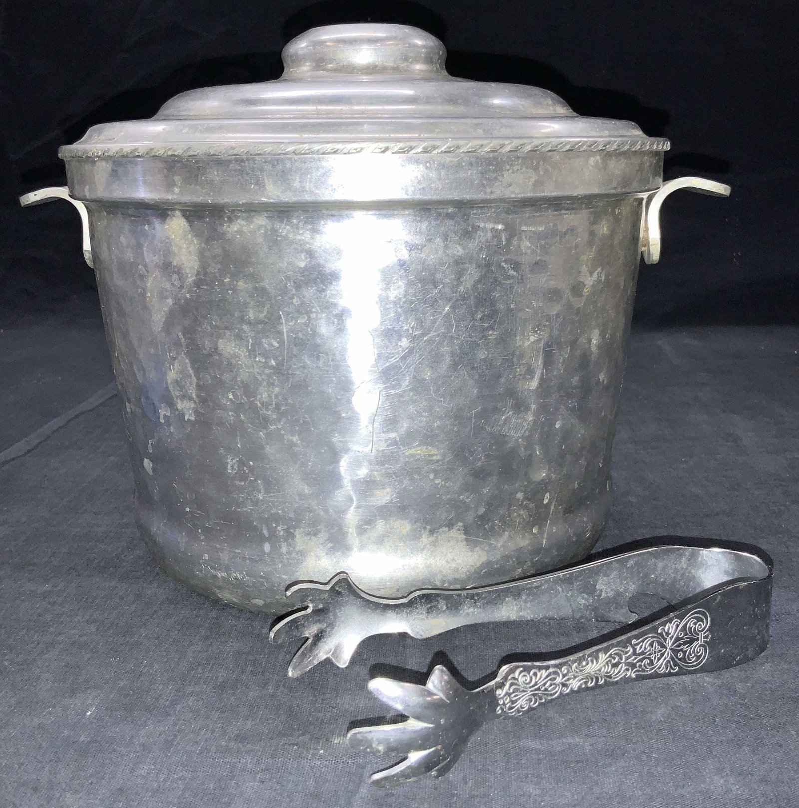 Vintage Aluminum Ice Bucket W Tongs: Vintage aluminum made ice bucket with etched white metal ice cube tongs. Bucket has curved side handles and braided accented rim. With hammered exterior No glass insert. Approximately 7.5 inches tall 