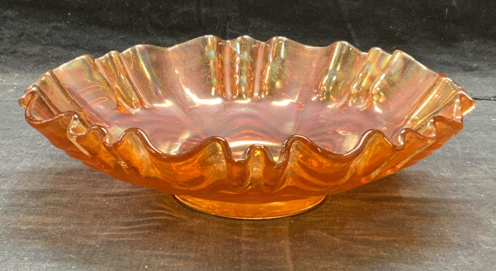 Orange Iridescent Carnival Art Glass Bowl: Orange iridescent carnival art glass bowl with handkerchief rim. Measures approx. 8 inches diameter and 2.75 inches tall. Some surface wear consistent with exposure. Carnival glass, carnival glass bow