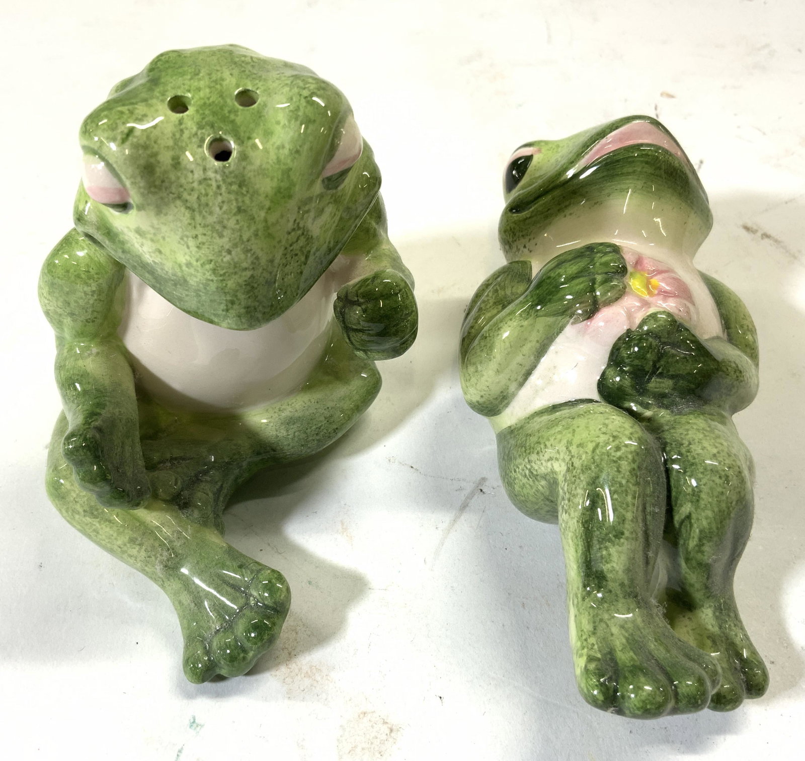Lot 2 Porcelain Frog Salt & Pepper Shakers: Lot includes 1 salt & 1 pepper shaker. One depicts a seated frog, one depicts a laying frog. Larger shaker measures approx 3.5 inches tall & deep, 2.75 inches wide. Salt & pepper shakers, frog salt an