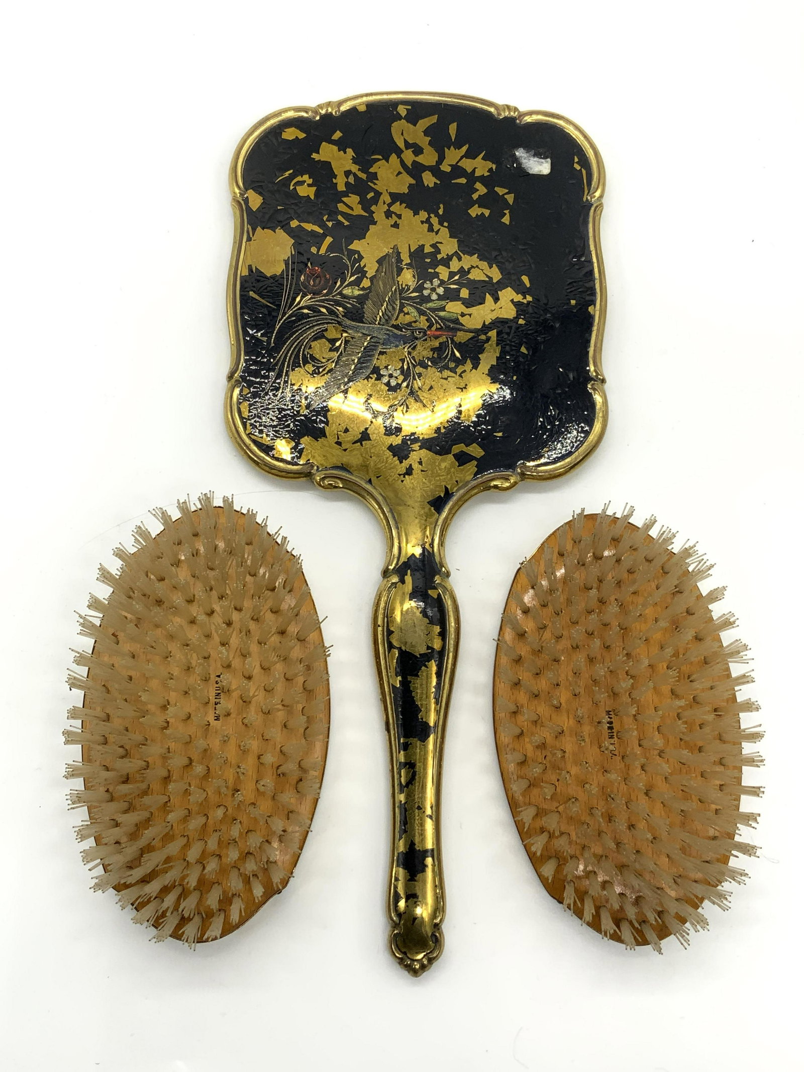 Lot 3 ELAIN AMERICAN Brushes & Vtg Hand Mirror: 2 Elain American wood and gold tone metal brushes. Made in USA. Trademarked to metal. Measure approx. 5 x 3 x 1.5 inches. Vintage gold tone metal hand mirror with enamel decoration and bird motif. Los