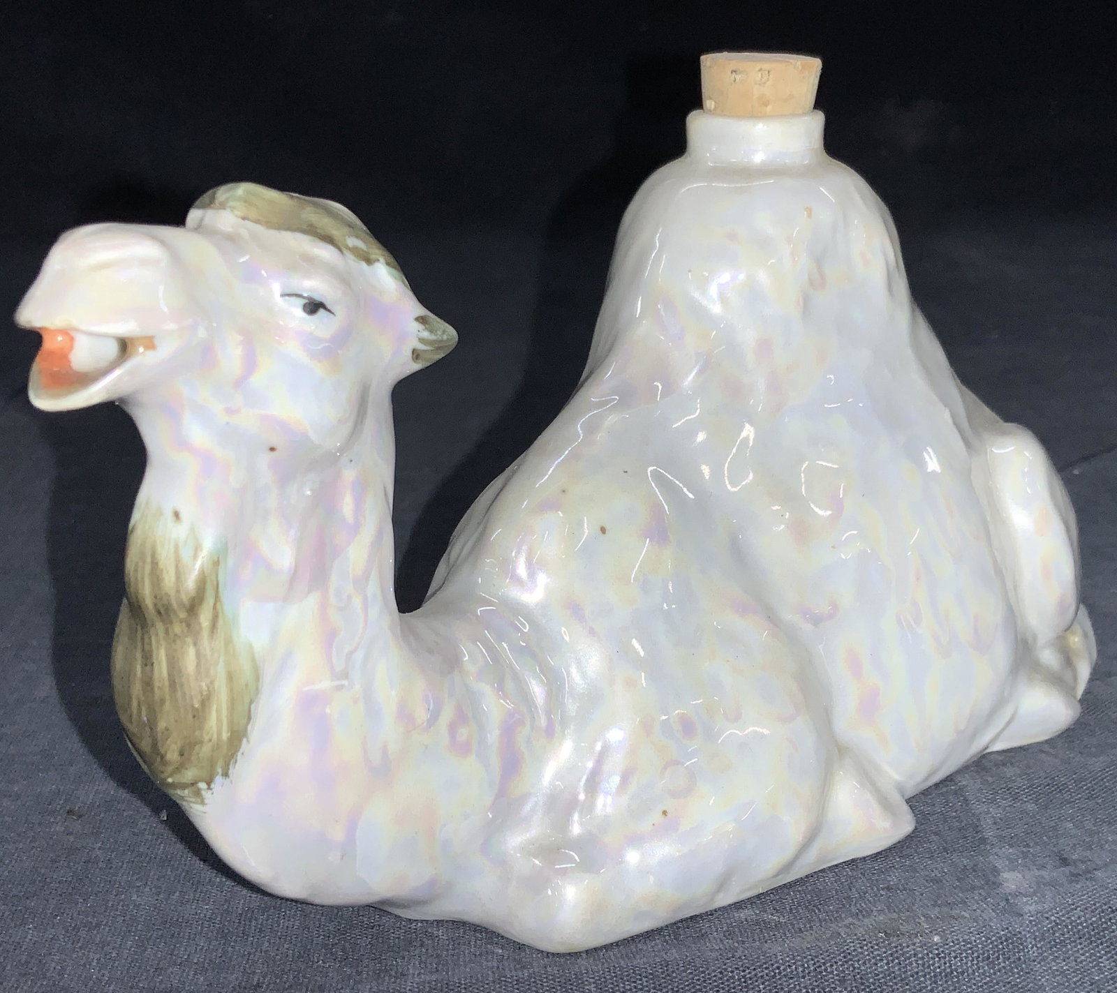 Porcelain Camel Bottle, Germany: Porcelain made camel bottle with cork topper and mouth of camel open for liquid to pour out. Marked on underside,Germany. Approximately 4 inches tall and 8 inches long. Moderate surface wearing due to