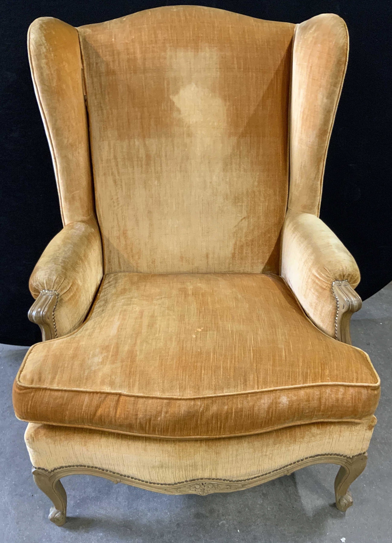 Vintage Country French Style Velvet Wing Chair: Country French style orange hued velvet wing chair. Carved floral motifs and carved scroll feet to the legs. Nailhead details. Measures approx 41H x 28D x 30W in. Some surface wear consistent with age