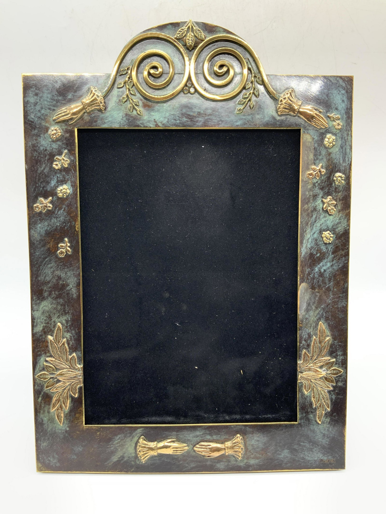 Bautista Stamped Patina Brass Picture Frame: Marked on lower right corner Bautista Brass made frame with raised floral motifs and hands in a spiral on top crown. Back panel is brown felt with easel backing. Approximately 13 x 10.5 inches, window