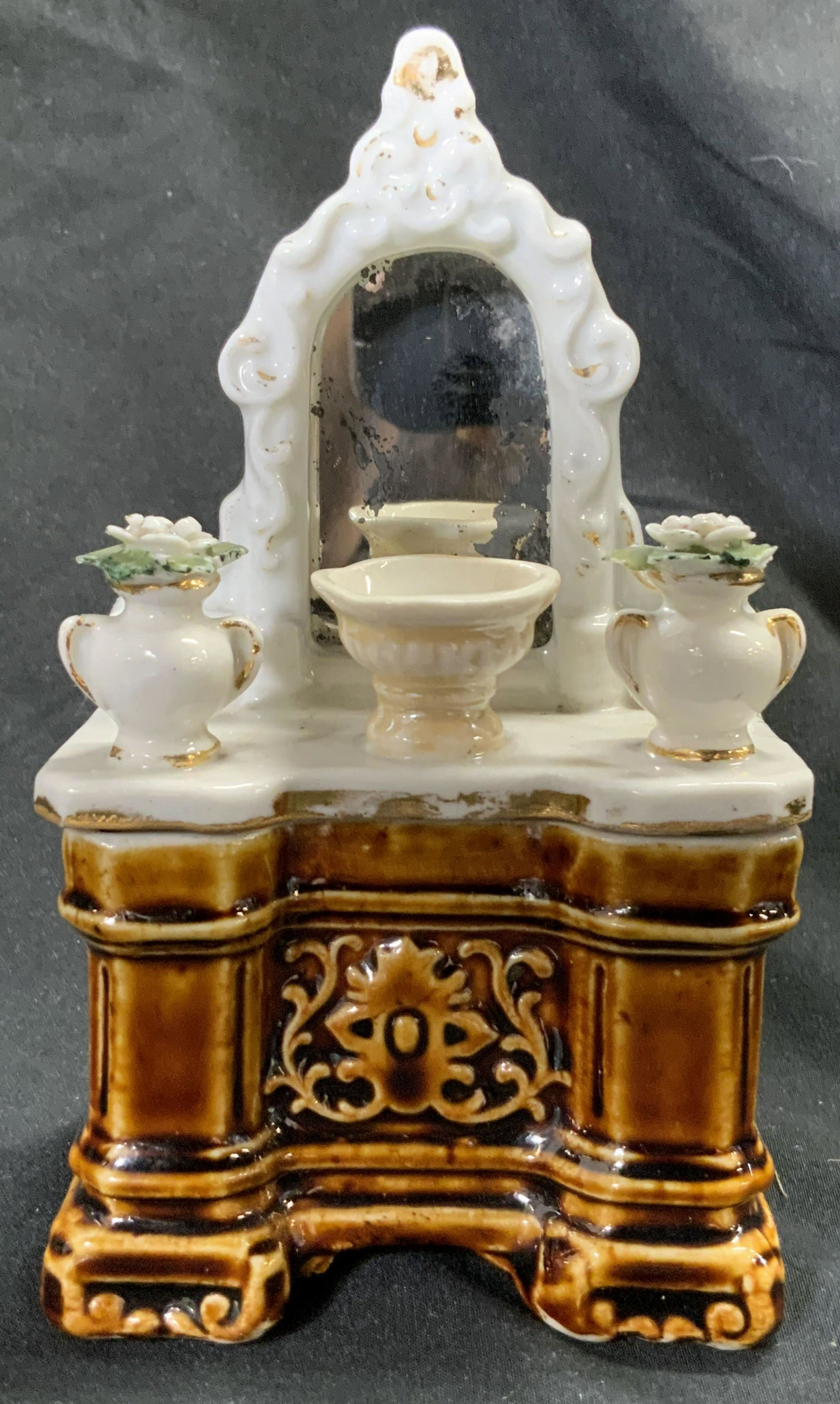Antique Porcelain Whimsey Vanity Trinket Box: Antique porcelain whimsey vanity trinket box. The lid features a mirrored vanity with a bowl & vases to the sides. Hand painted and raised porcelain details throughout. Base is glazed brown, raised de