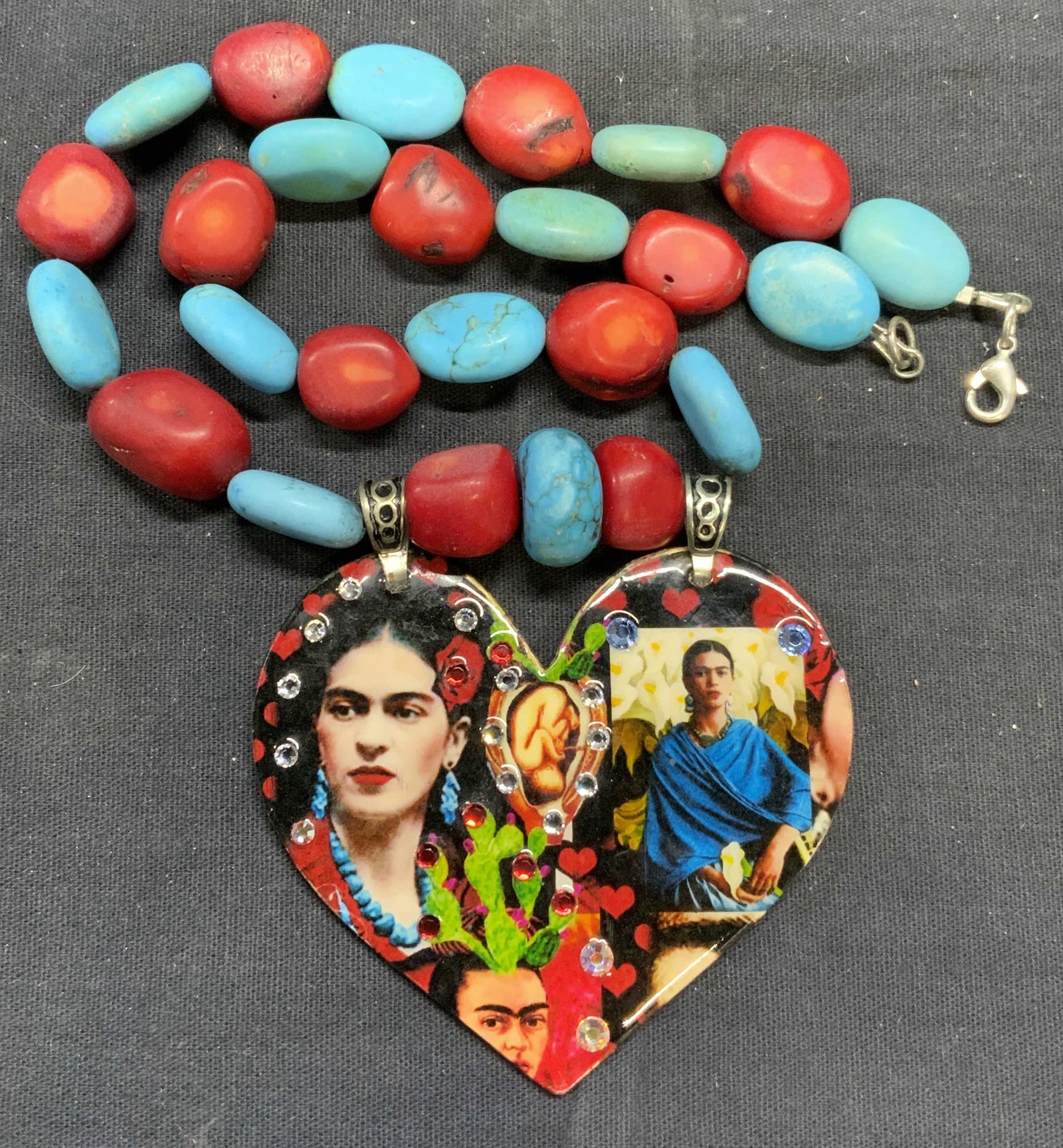 Turquoise & Coral Frida Kahlo Pendant Necklace: Signed artisan turquoise and red coral beaded necklace with heart shaped bejeweled Frida Kahlo pendant. Necklace measures approx. 18 inches long. Pendant measures approx. 2 7/8 x 2.5 inches. Signed to