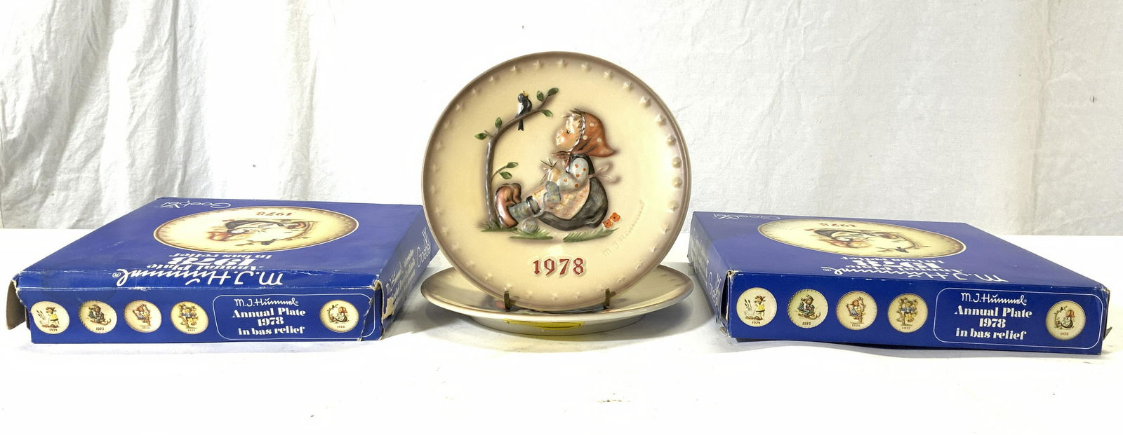 Lot 2 MJ HUMMEL GOEBEL HAPPY PASTIME W Boxes: Lot includes 2 plate. Each are MJ HUMMEL HAPPY PASTIME annual plate. Plates are each porcelain. Each piece is includes original box and pamphlets. Each plate measures approx 7.5 inches diameter. Plate