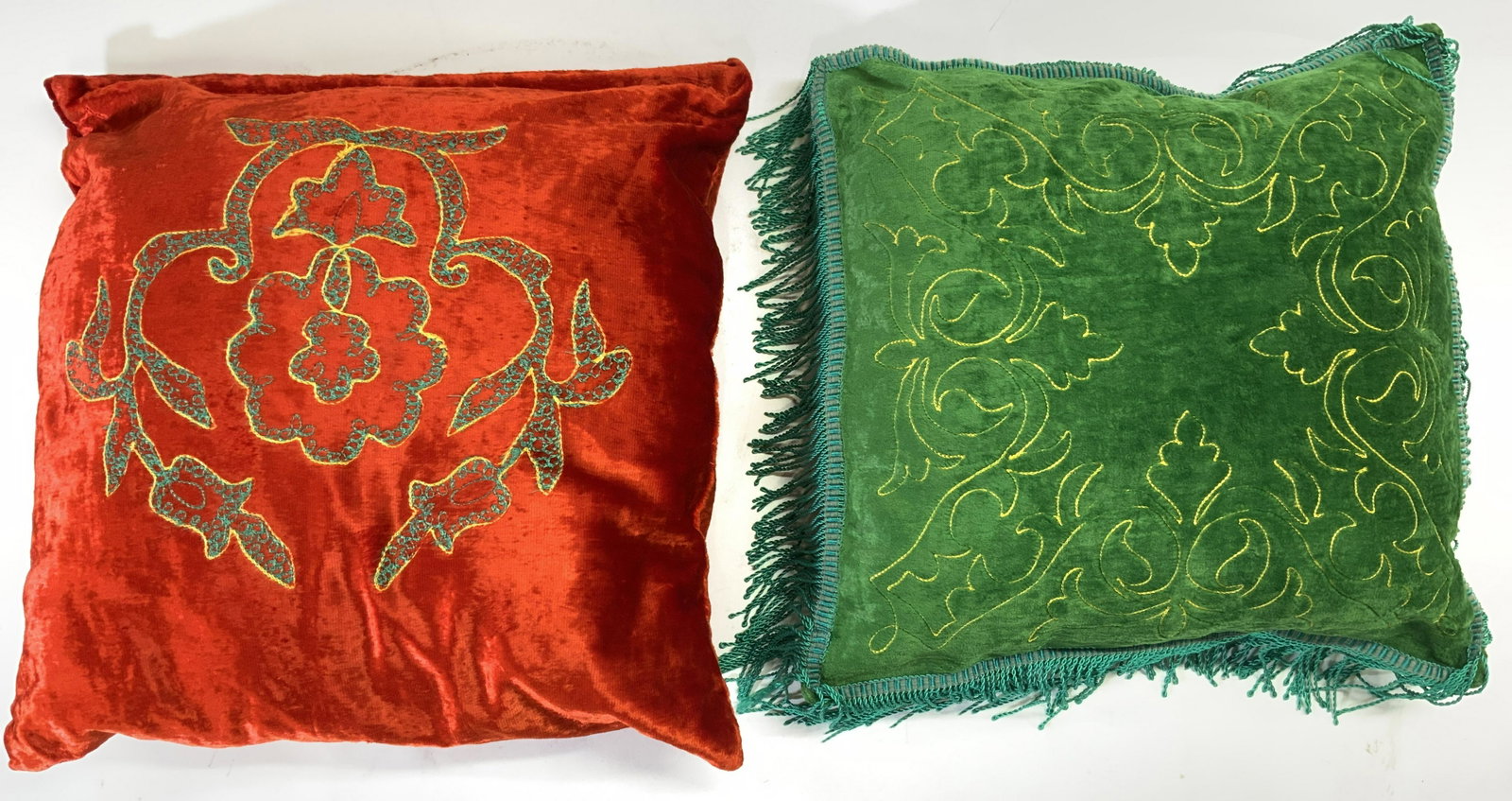 Lot 2 Crushed Velvet Pillows Green & Red: Lot includes 1 green & 1 red pillow. Each pillow appears to be upholstered with crushed velvet. Green pillow has fringes at edges. Each pillow has embroidered leaf detail. Pillows measure approx 16 in