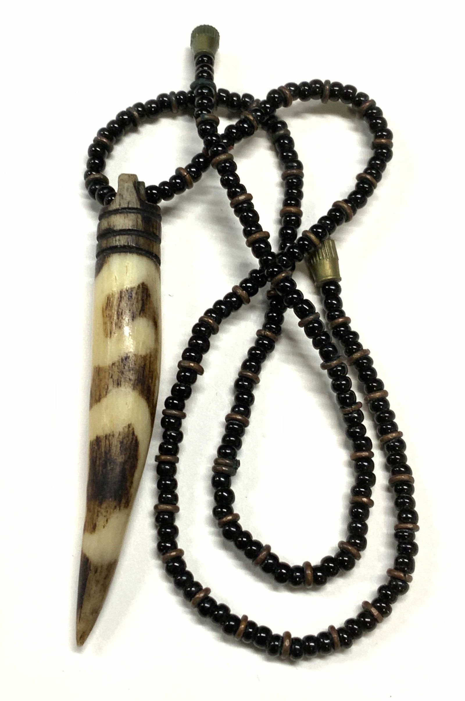Vintage Carved Bone Seed Bead Necklace: Vintage carved bone pendant necklace with black seed beads and brass beads. Some surface wear consistent with exposure. Measures approx. 17 inches long. Pendant measures approx. 2 5/8 x .5 inches. Est