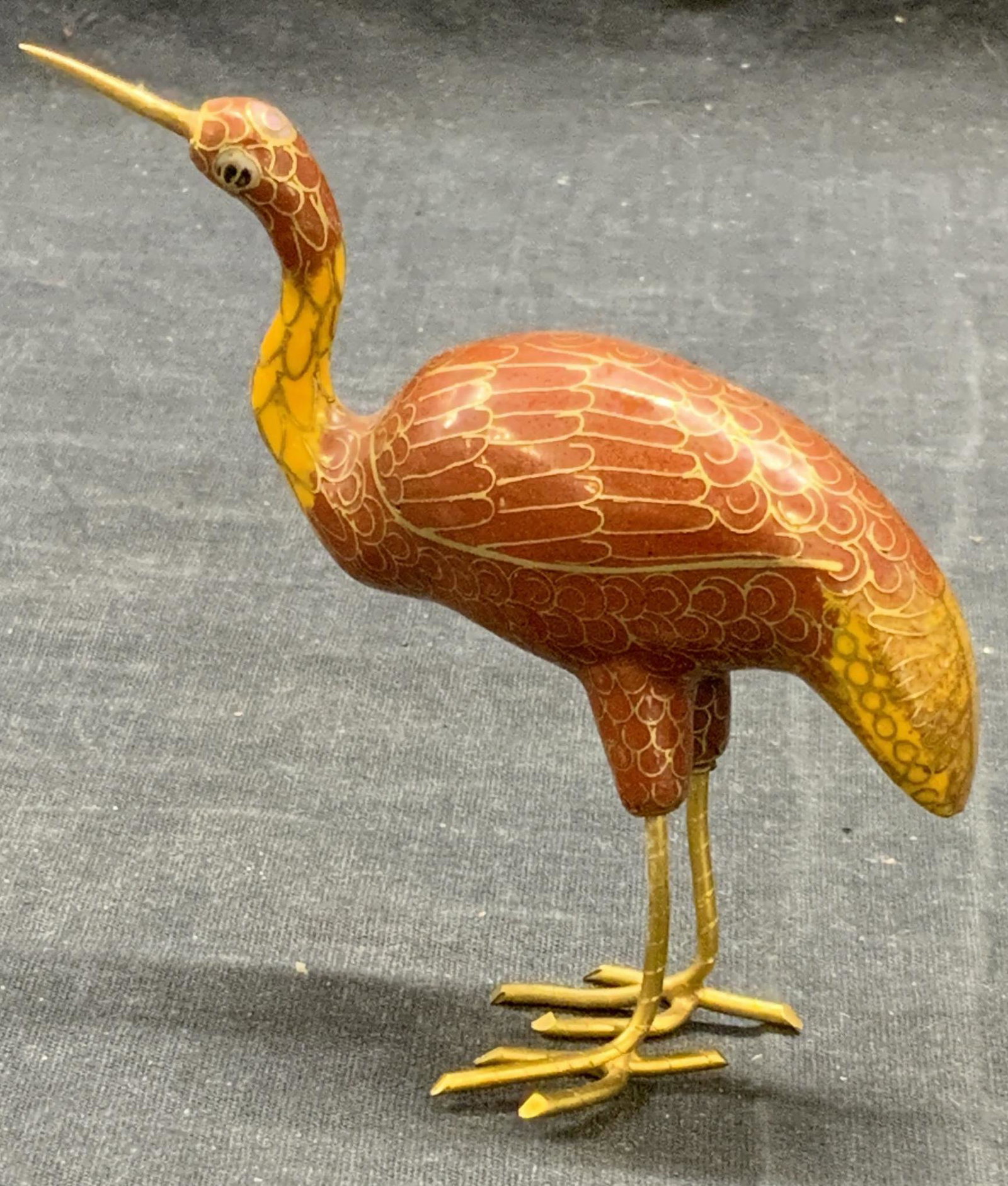 Red/Orange Cloisonne Crane Figurine: Red and orange toned gilt cloisonne crane figurine. Enamel over metal. One leg is loose. Measures approx. 4 x 1 x 4.25 inches. Cloisonne crane, crane figurine, cloisonne figurine, crane, bird figurine