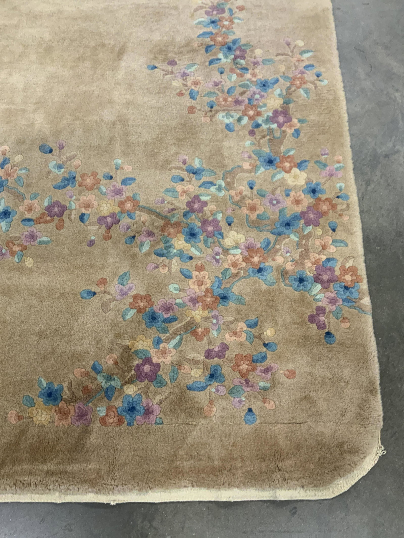 Vintage Chinese Art Deco Style Floral Rug: Vintage Chinese art deco style rug. Primarily beige hued with pops of colorful florals. Rounded edges. Piece appears to be crafted from wool. Measures approx 130L x 106W in. Some surface wear present.