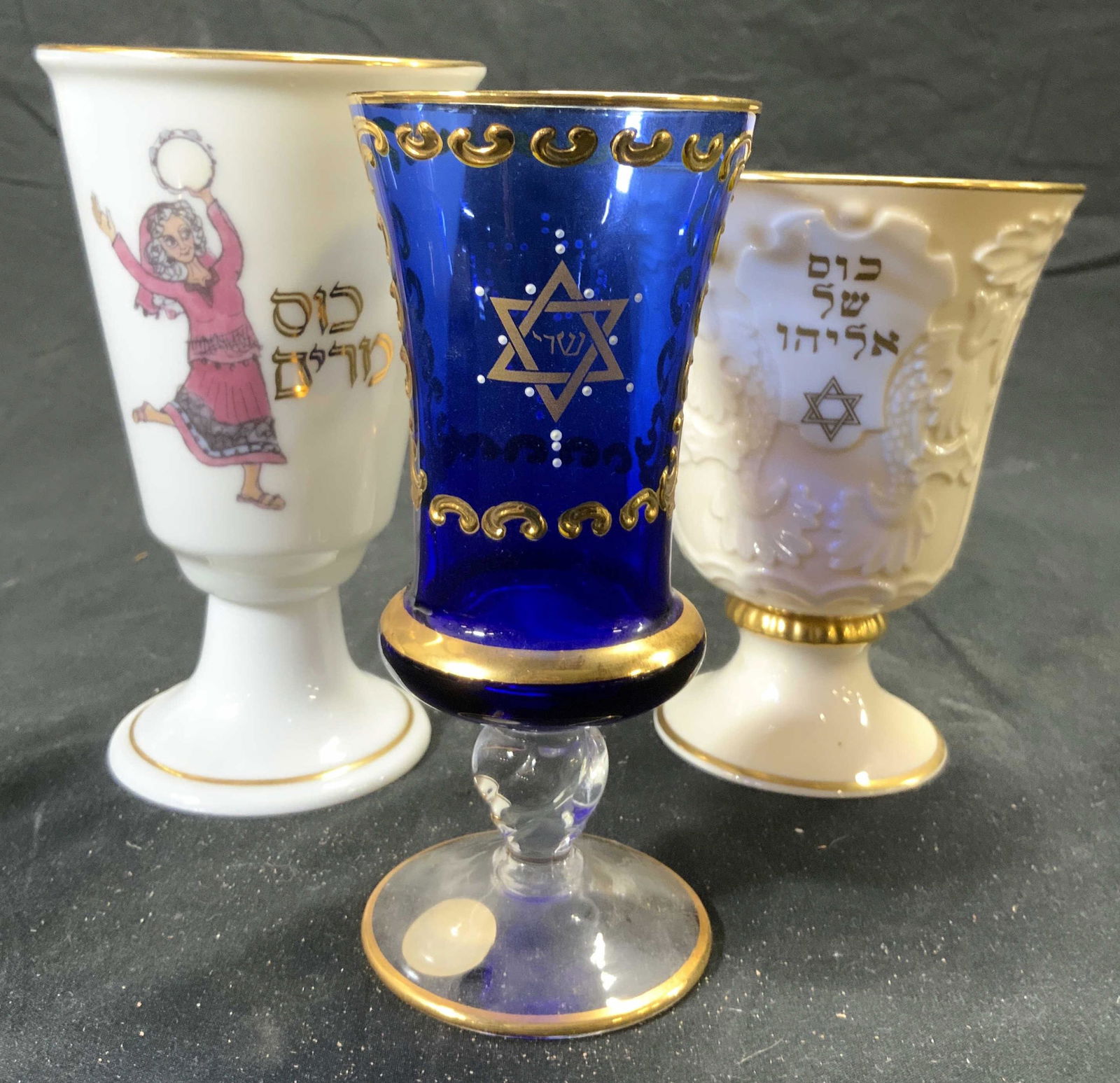 Lot 3 Judaica Passover Cups, Murano, Lenox, More: Lot includes 3 Passover cups goblets. Each have Hebrew characters. 1 has tag which reads MURANO GLASS MADE IN ITALY is cobalt blue glass with gilt detail, 1 is LENOX cream toned porcelain with gilt ri