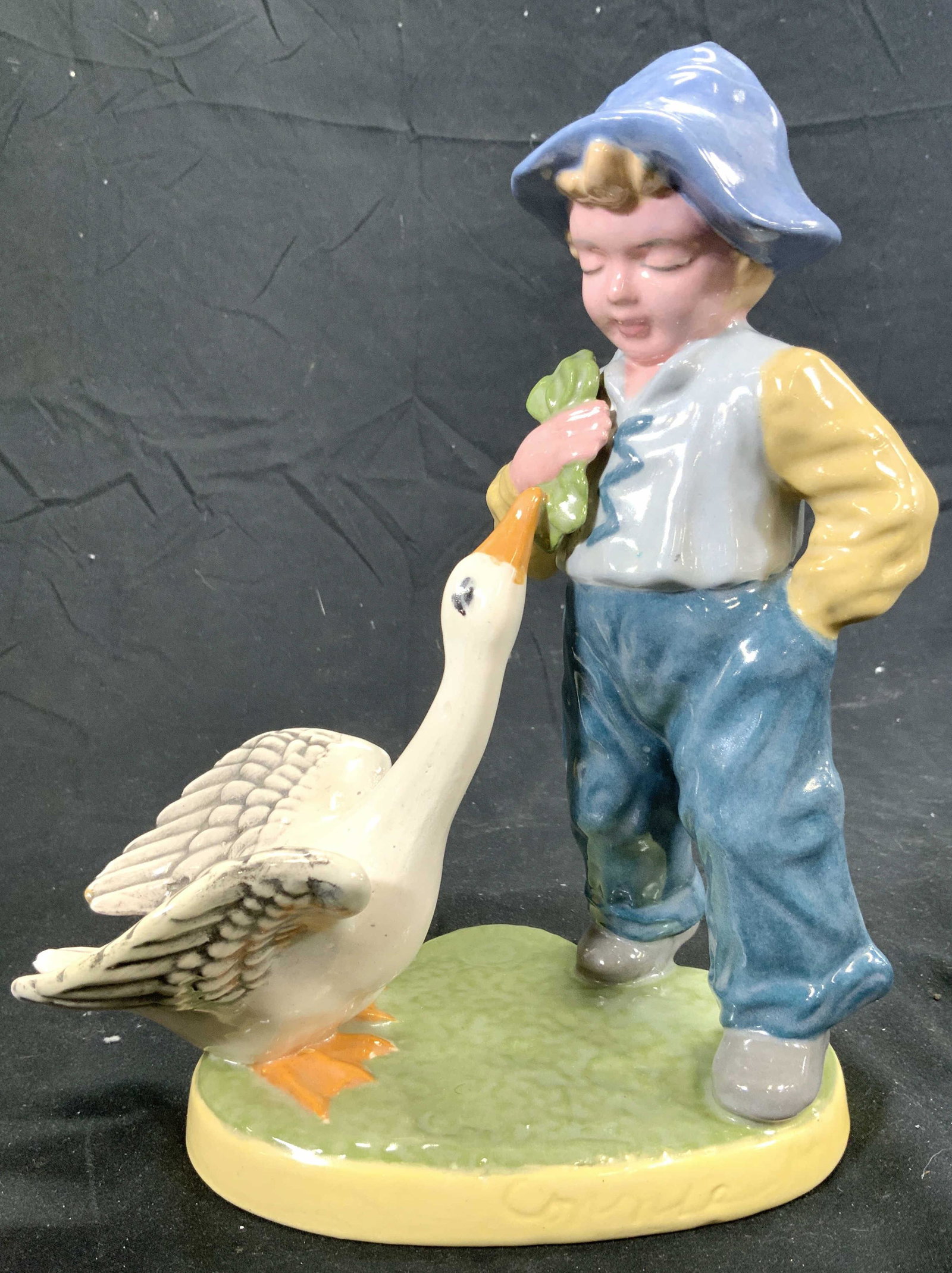 Signed Porcelain Dutch Boy W Goose Figure: Signature appears to reads CORNIA. Piece is vintage. Depicts a Dutch boy figure with goose figure on green base. Piece is possibly hand crafted. Measures approx 9 inches tall 7 inches wide 4.5 inches 