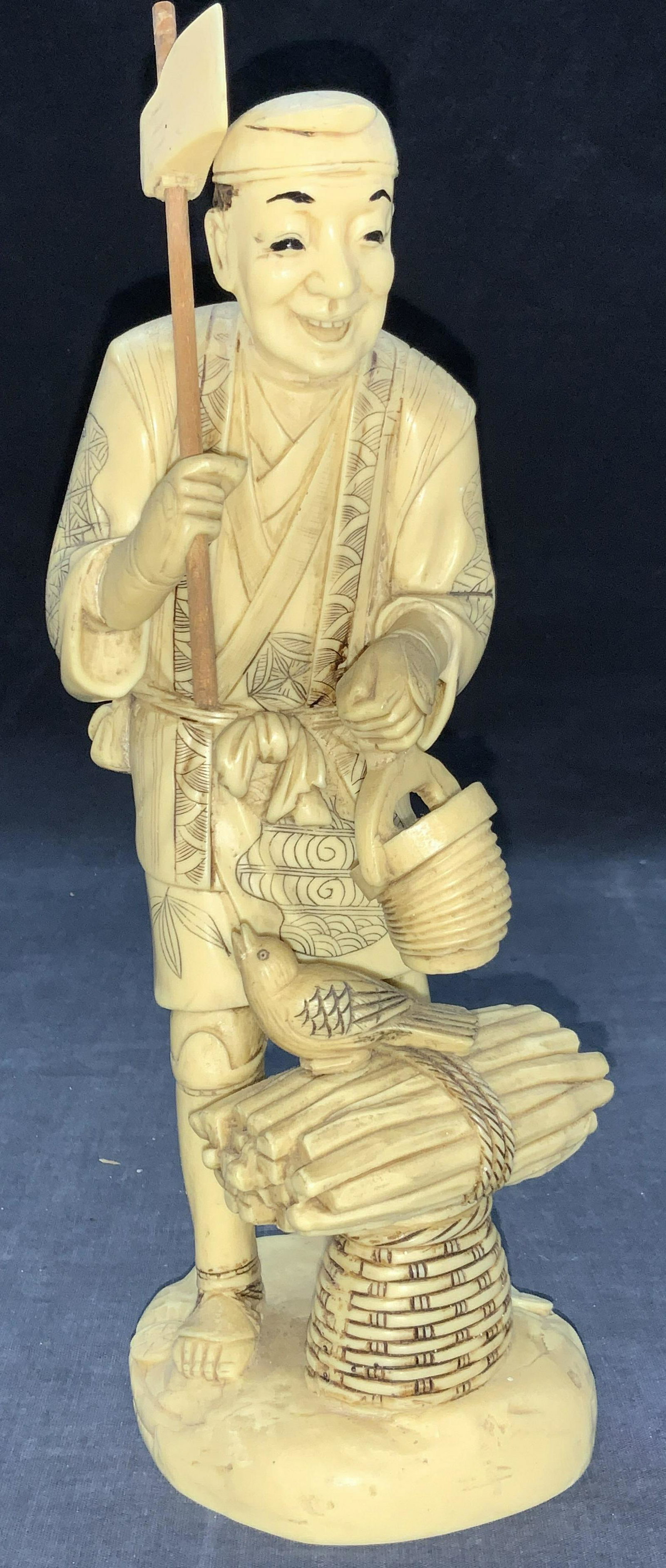 Resinous Carved Asian Wood Cutter Sculpture: Carved resin made sculptures of a Japanese wood cutter. Depicting a man in intricately carved robes holding an axe in one hand and a lantern in the other with bundle of sticks in front of him with a b