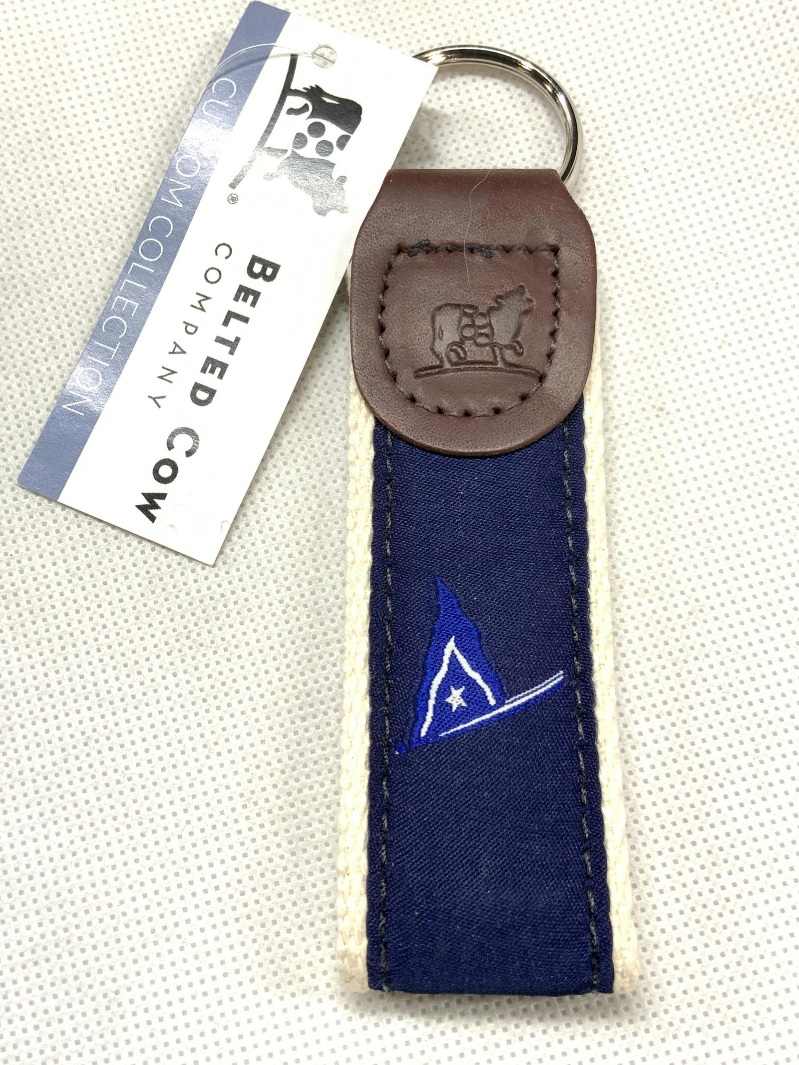 Belted Cow Ribbon Keychain NWT: Ribbon keychain with blue sailing flag with leather end with Belted Cow Logo imprinted. Comes with tag that reads Belted Cow Custom Collection. Approximately 5 inches long. Never used. Ribbon key chai