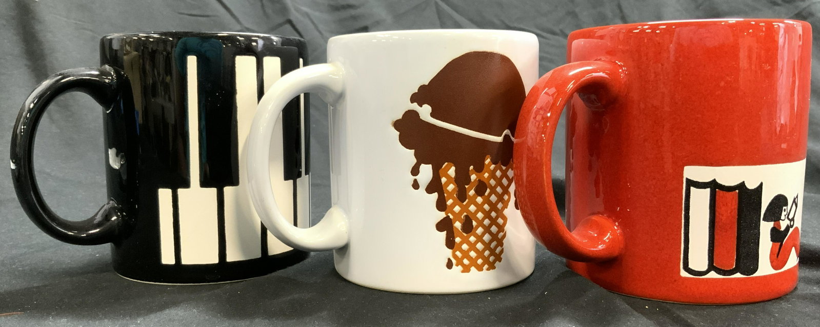 WAECHTERSBACH Lot 3 Porcelain Mugs Vessels: Undersides of 2 mugs read WAECHTERSBACH W GERMANY underside of one reads SPAIN. Lot includes 1 red mug depicting a seated female figure reading & books, 1 white mug with ice cream cone detail, & 1 bla