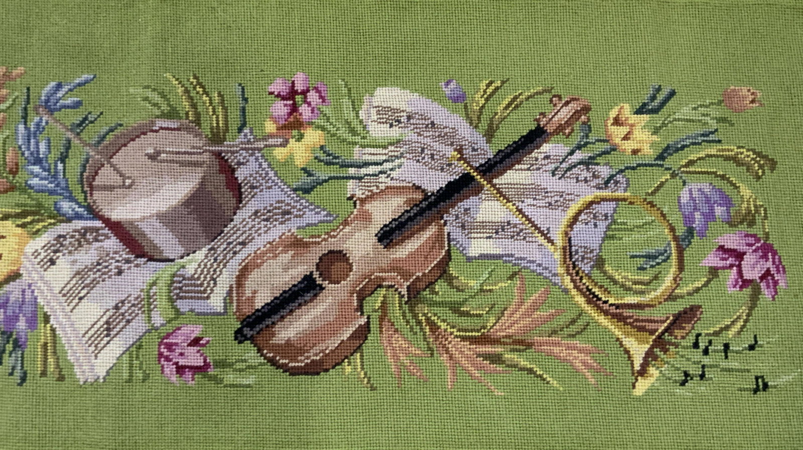 Vintage Handmade Musical Motif Needlepoint: A vintage handmade musical motif needlepoint. Green background featuring musical instruments, sheet music, and florals to the center. Instruments include a drum, a violin, and a trumpet. Measures appr